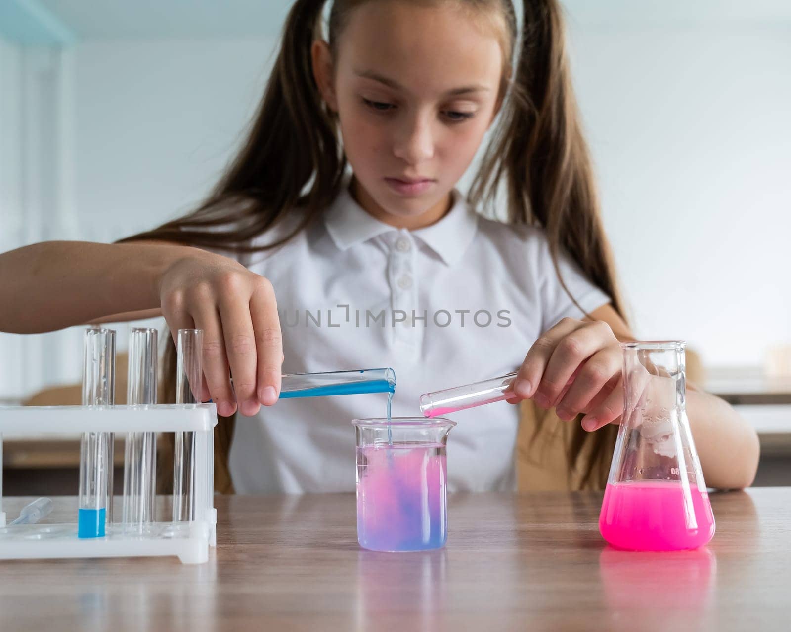 A schoolgirl conducts experiments in a chemistry lesson. Girl pouring colored liquids from a beaker. by mrwed54