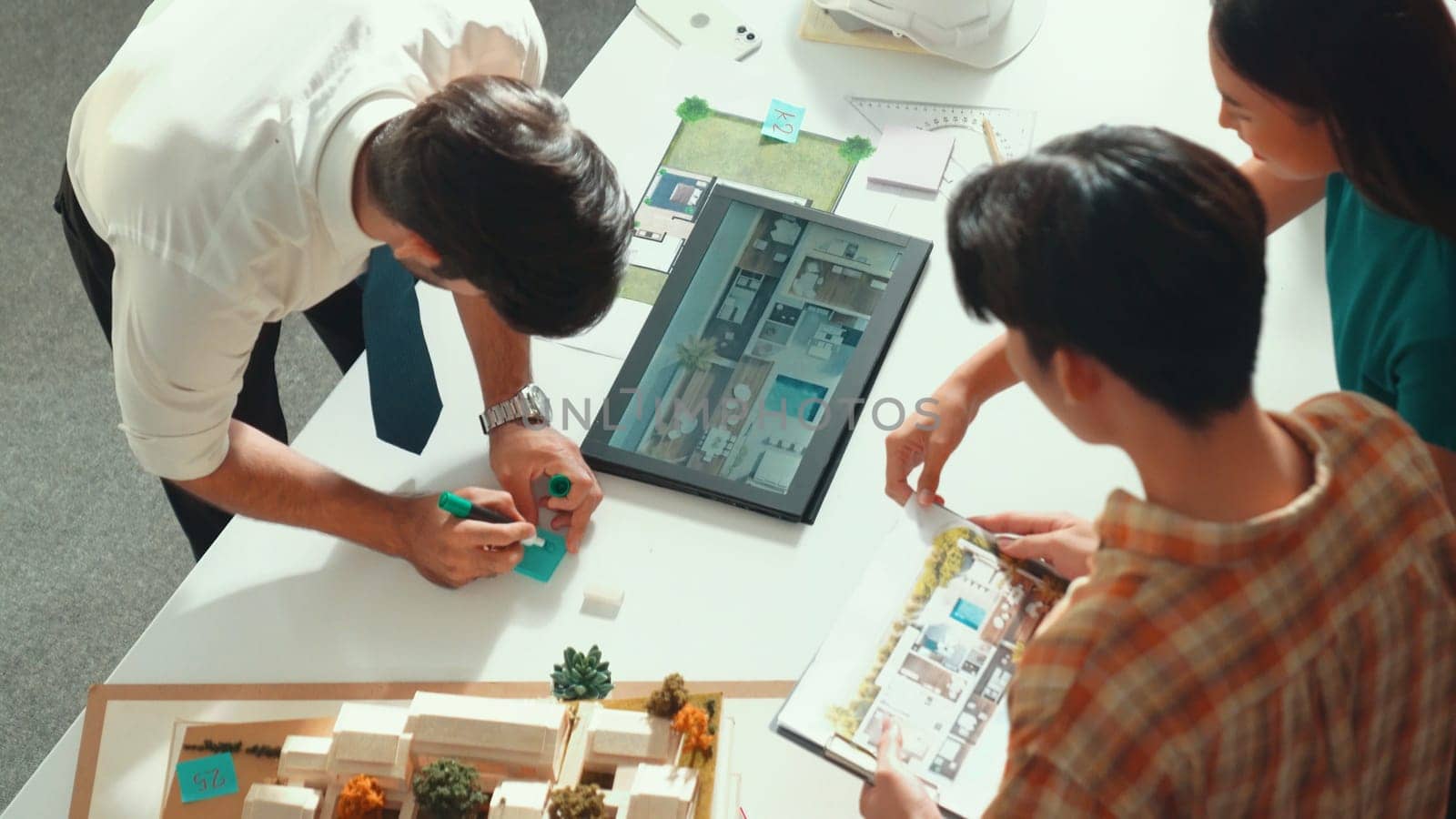 Top down view of manager pointing at house model and explain building design. Aerial view of architect engineer brainstorming about interior construction while tablet display house plan. Alimentation.