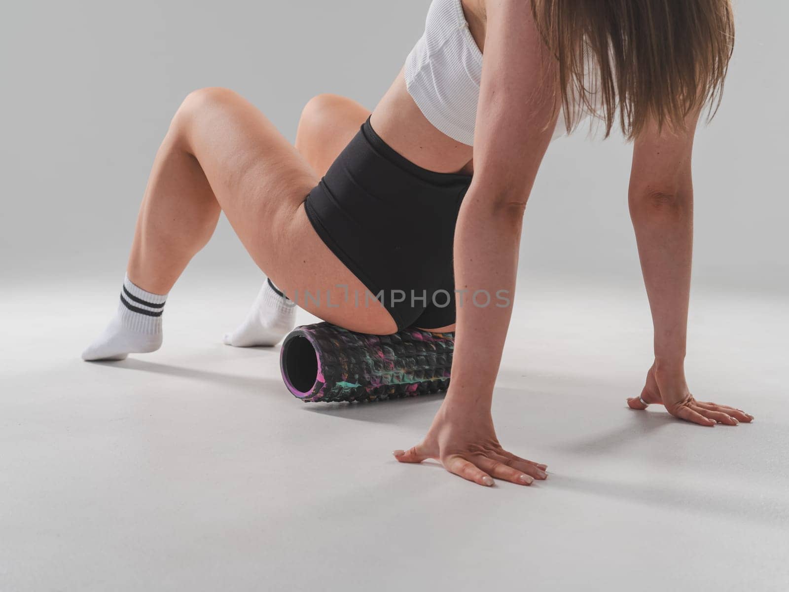 Faceless woman doing roller exercise for myofascial release on white background. Self-massage of thighs