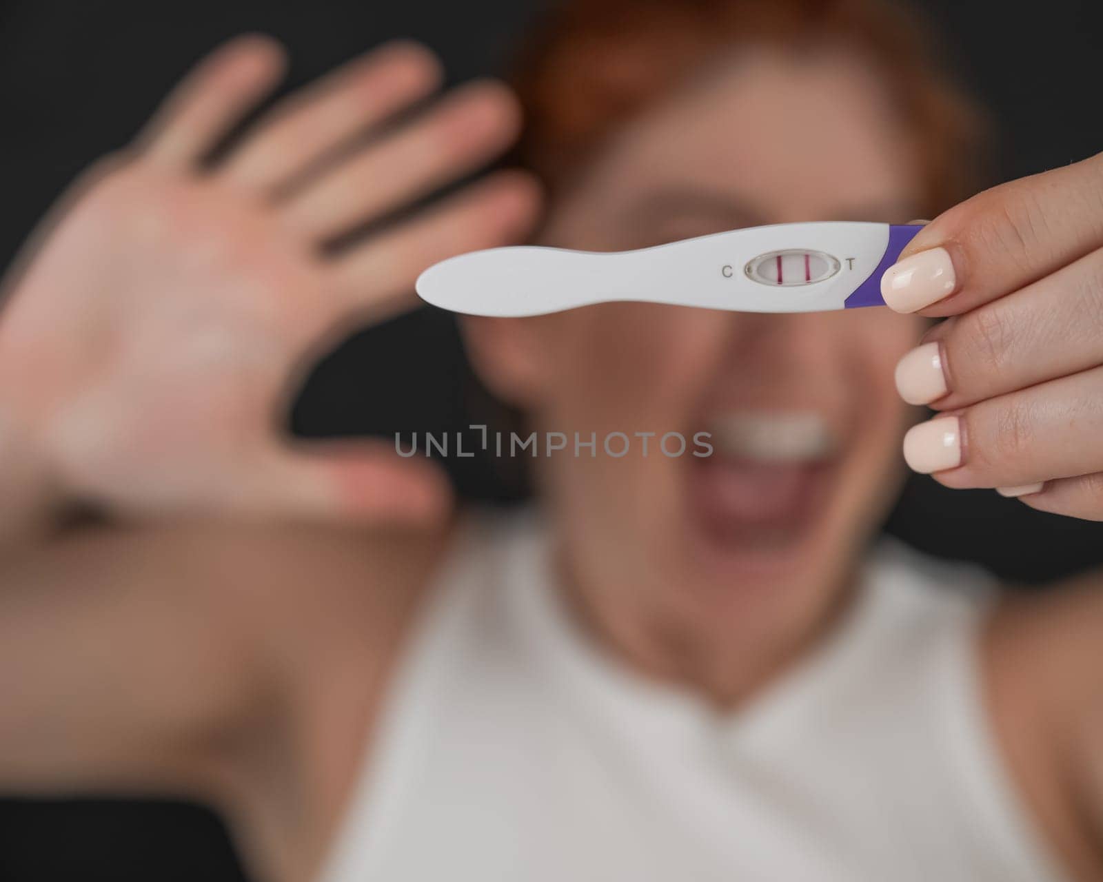 Blurred portrait of upset caucasian woman holding positive rapid pregnancy test on black background