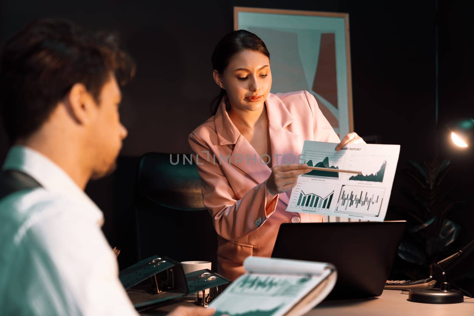 Focusing on sitting on pink suit woman presenting graph target on paperwork to explain customer market target graph report's business expansion to coworker while man holding paper to sign. Postulate.