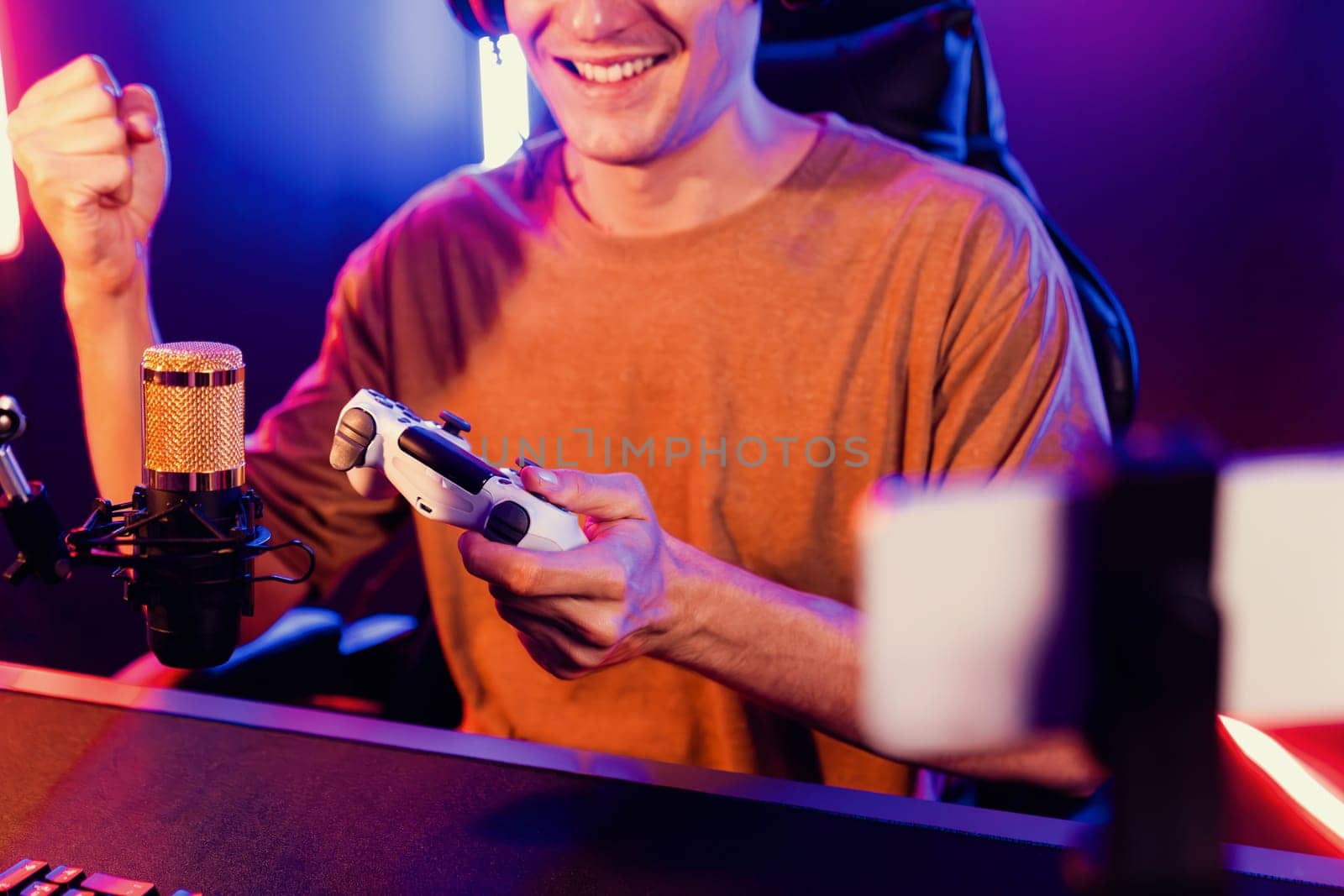 Enjoy smart gaming streamer with control joystick, playing game online of live streaming by smartphone rec with team skilled players on computer at modern technology cyber neon light room. Pecuniary.