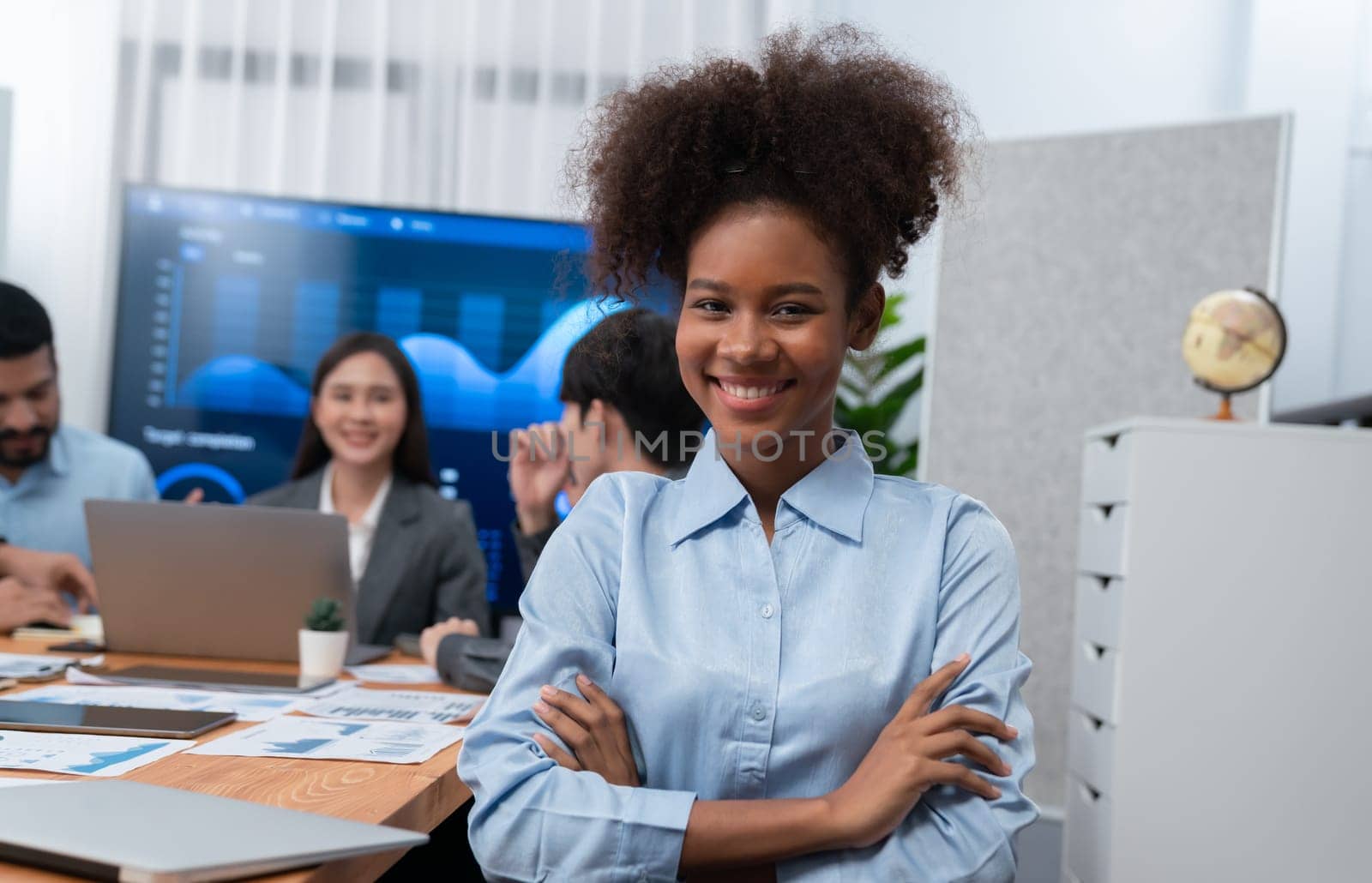 Portrait of happy young african businesswoman with group of office worker on meeting with screen display business dashboard in background. Confident office lady at team meeting. Concord