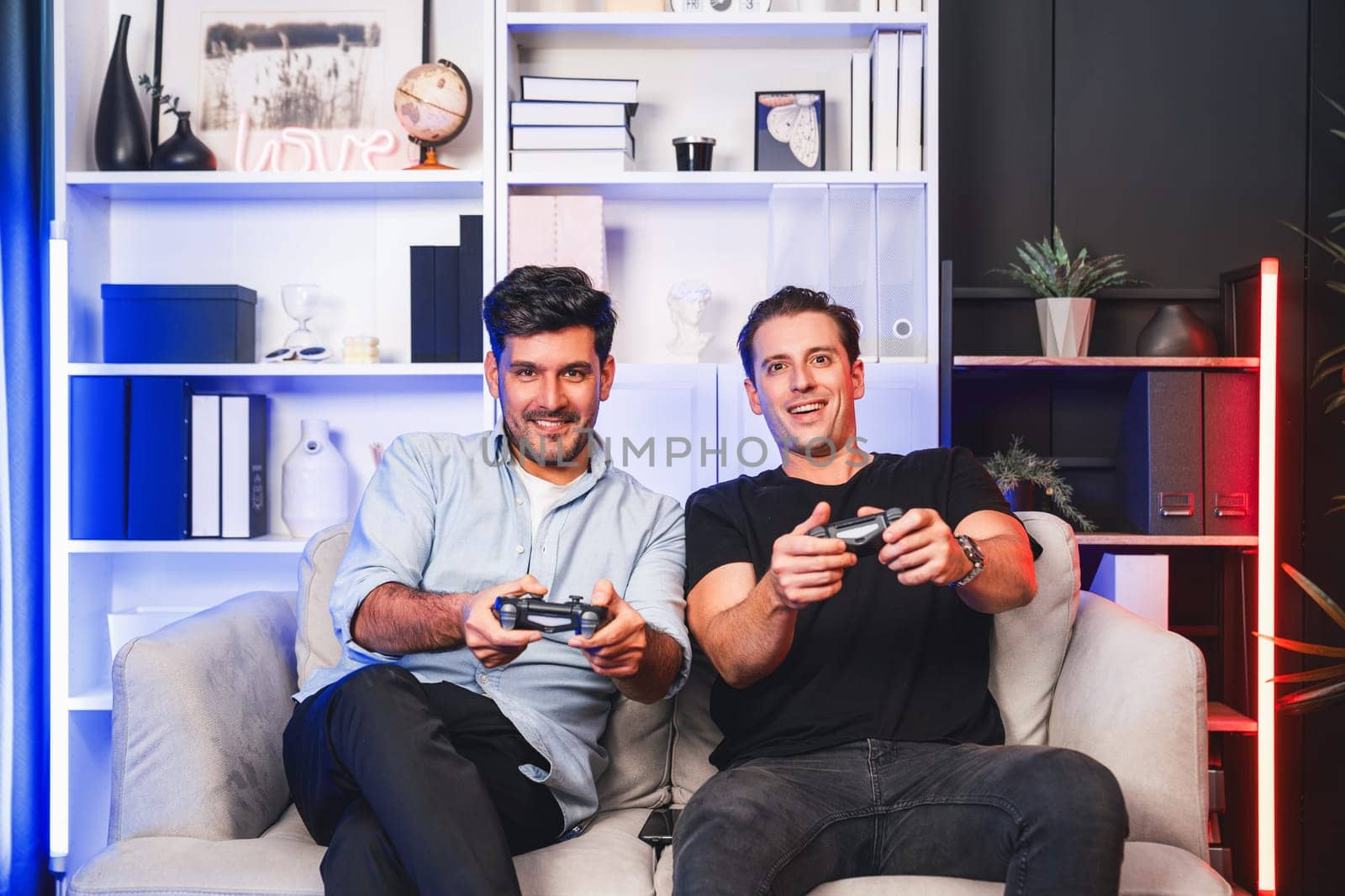 Winner and loser players of buddy friend gamers playing video game on TV using joysticks in studio room with neon blue light. Comfy living indoor at home place with cheerful fighting winner. Sellable.