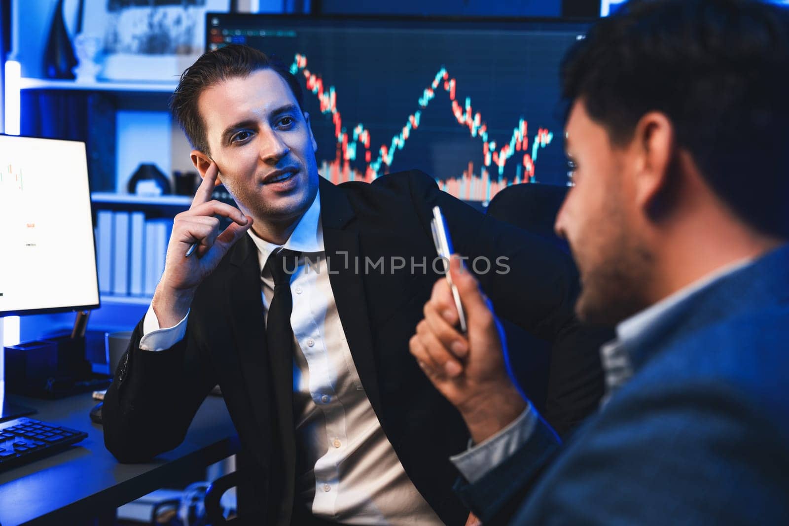 Two stock exchange traders discussing on dynamic investment graph, trending of high profit in currency stock. Showing financial benefit data on monitor screen in neon light at workplace. Sellable.