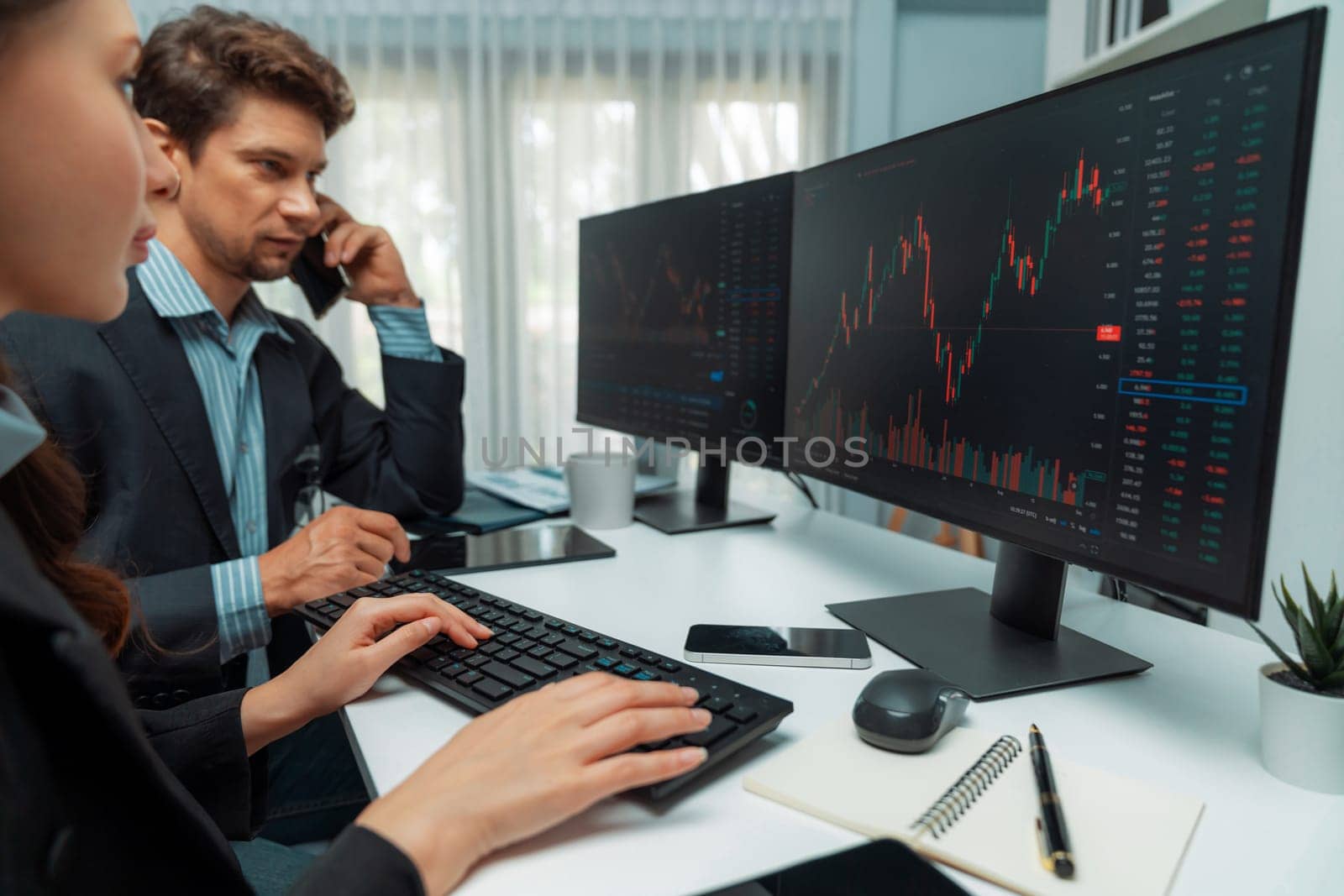 A man broker calling trader businessman to inform high profit point of stock exchange in digital currency while a woman assistance pointing to analyzed data monitor on real time at office. Postulate.