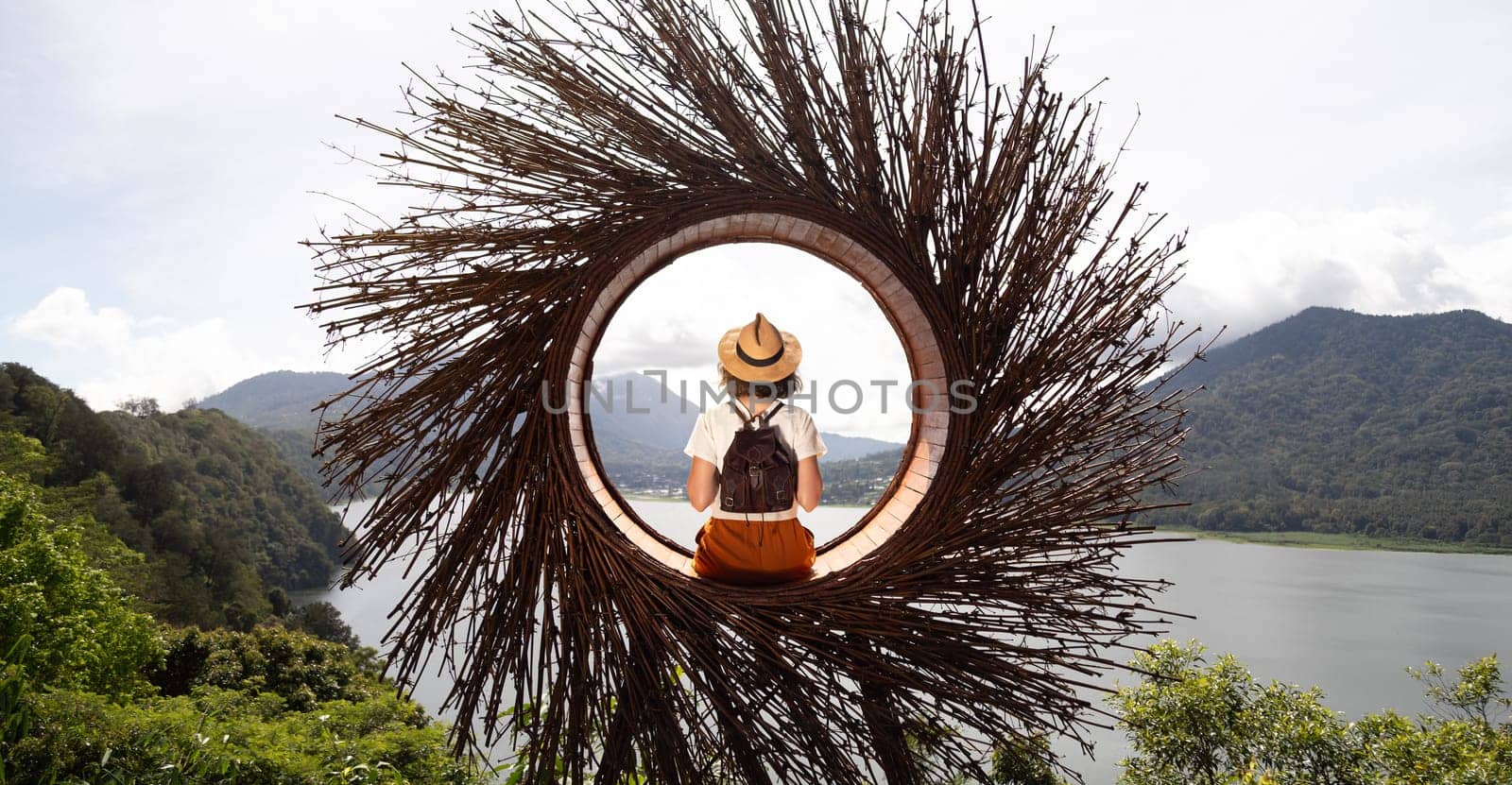 Female traveler contemplating nature sitting in straw nest looking at lake view in Munduk, Bali. Banner image. Travel, vacation concept.