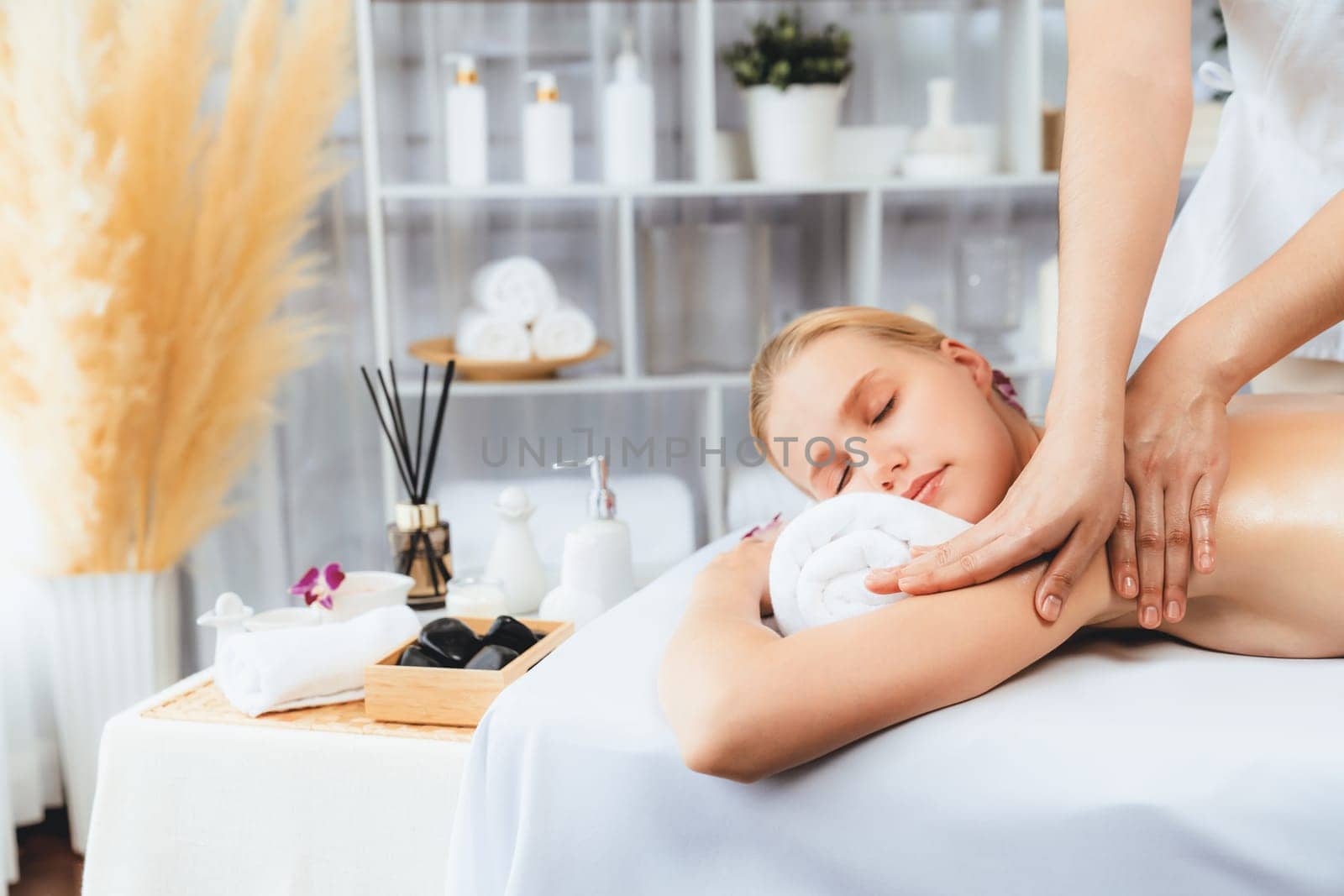 Caucasian woman customer enjoying relaxing anti-stress spa massage and pampering with beauty skin recreation leisure in day light ambient salon spa at luxury resort or hotel. Quiescent