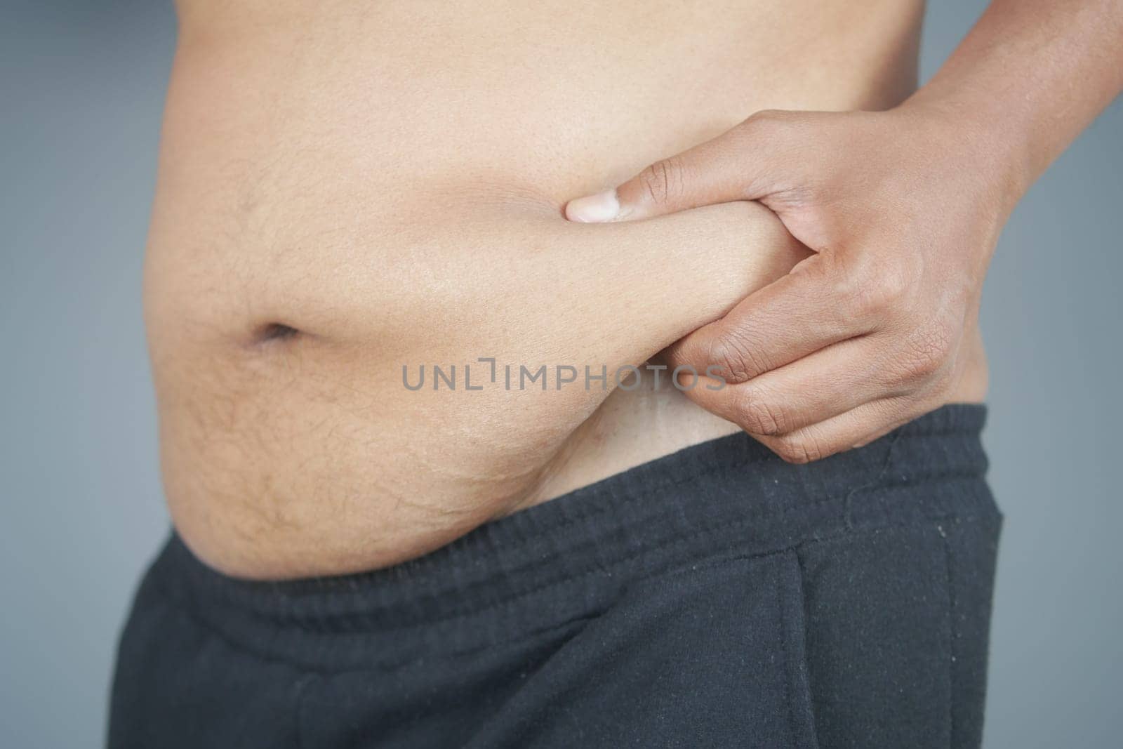 man's hand holding excessive belly fat, overweight concept.