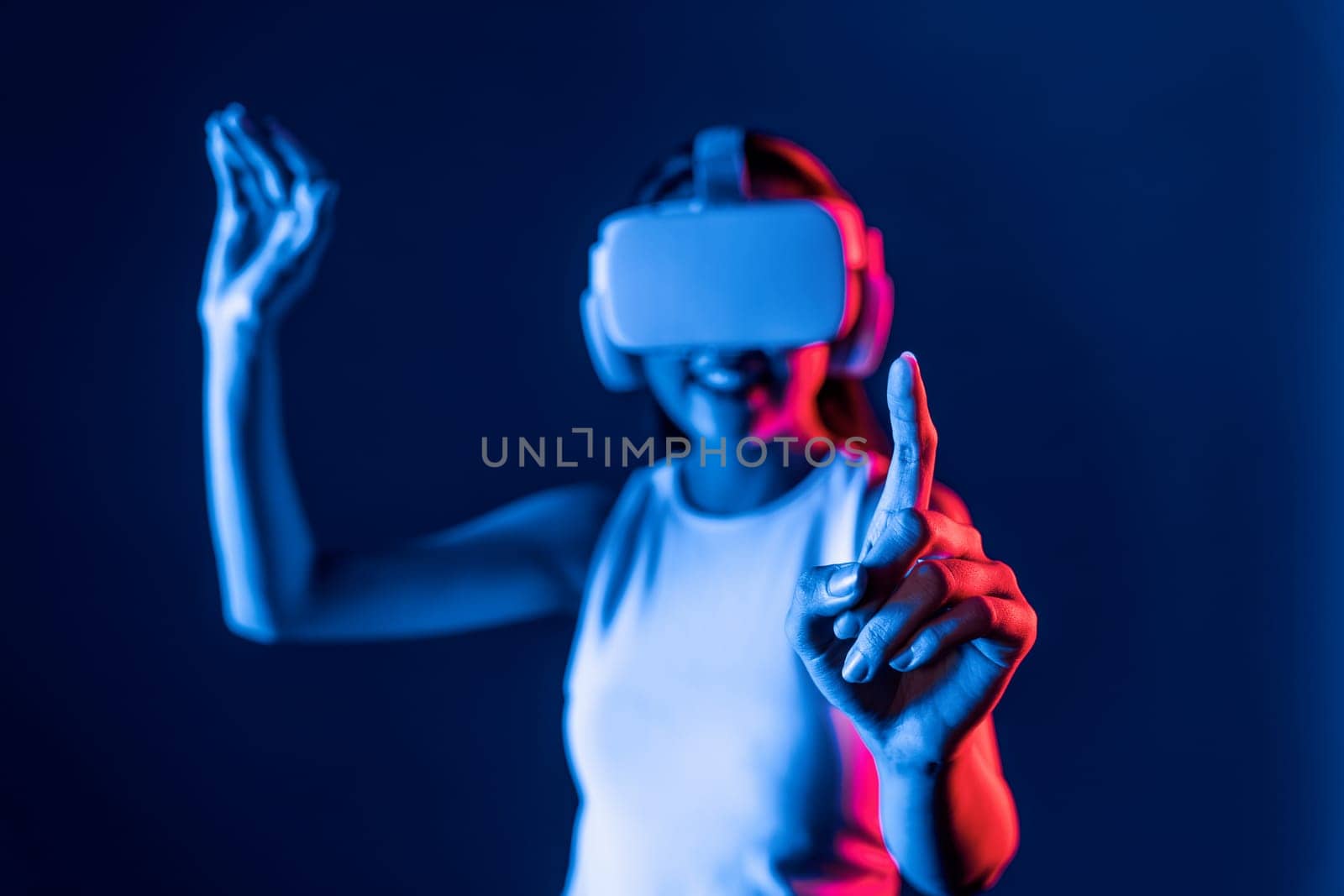 Smart female stand with surrounded by cyberpunk neon light wear VR headset connecting metaverse, futuristic cyberspace community technology. Woman using finger pointing virtual object. Hallucination.