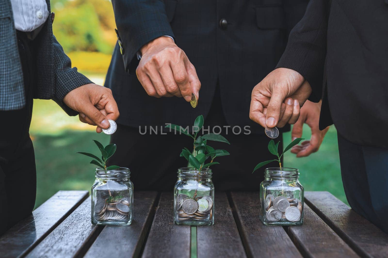 Business people put coin to money saving glass jar on outdoor table as sustainable money growth investment or eco-subsidize. Green corporate promot and invest in environmental awareness. Gyre