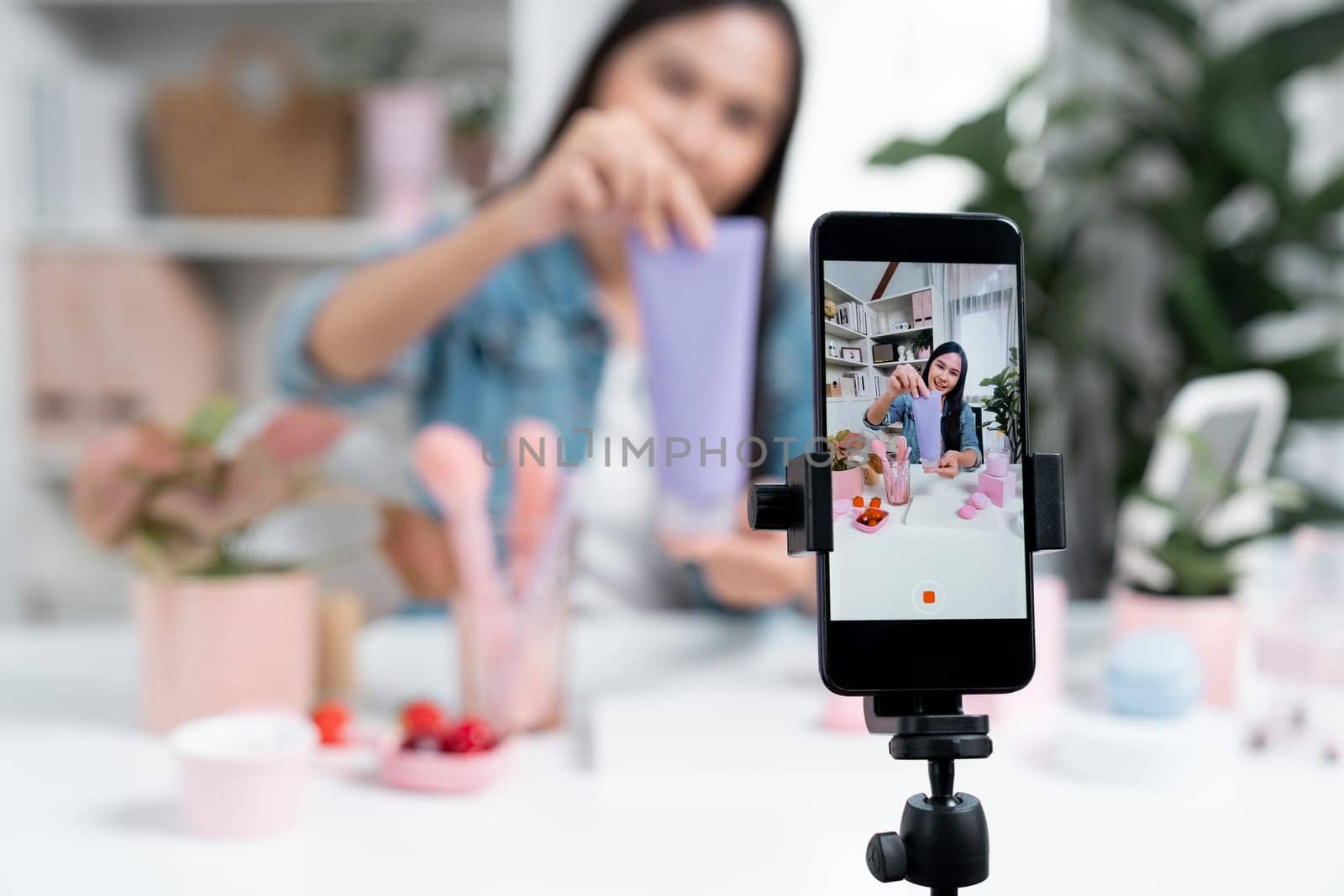 Selective focus phone with young beautiful Asian girl reviewing moisturizing body lotion cream product to make glow skin testing with arm on social media online live record with bestseller. Stratagem.