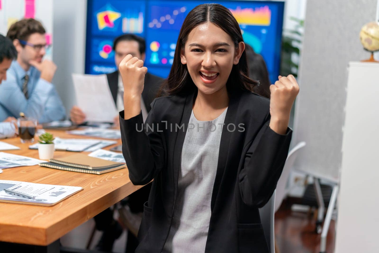 Portrait of happy young asian businesswoman or analyst looking at camera with her colleague analyzing data analysis in dynamic business strategy investment planning meeting. Meticulous