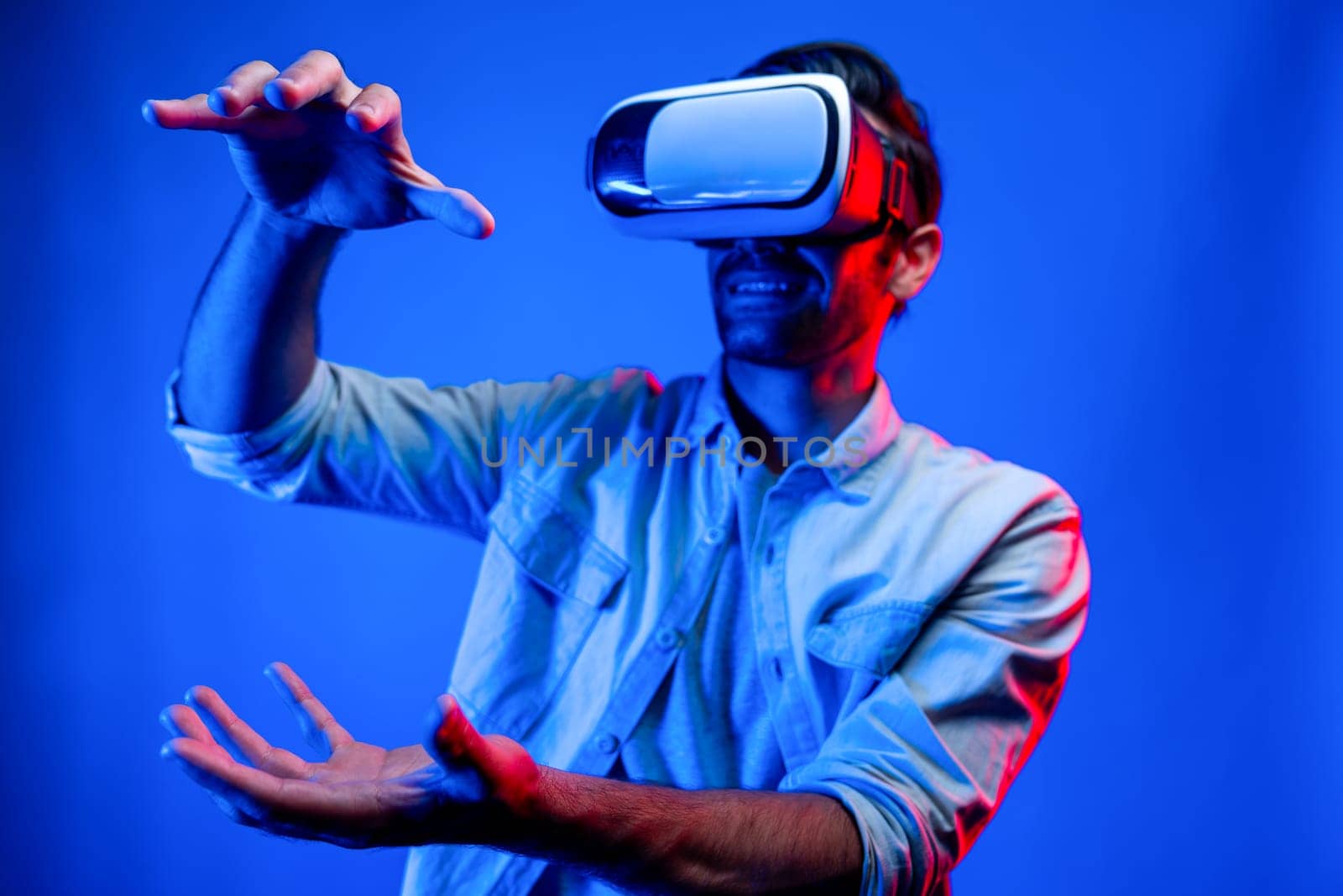 Caucasian smart man holding and moving gesture while using VR goggle. Happy person using headset and goggle while enter virtual world or metaverse with neon light background. Technology. Deviation.