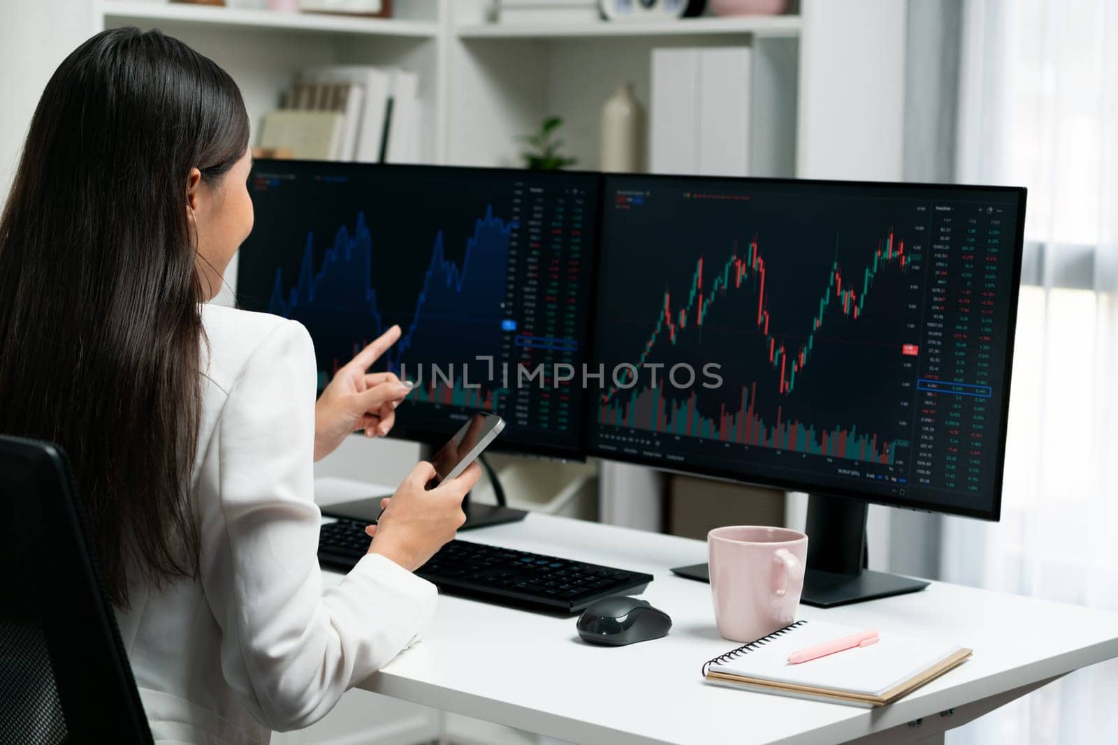 Young beautiful Asian businesswoman looking on pc to analyze profitable of exchange stock market graph at modern office. Concept of investing high profit in wealth security in finance. Stratagem.