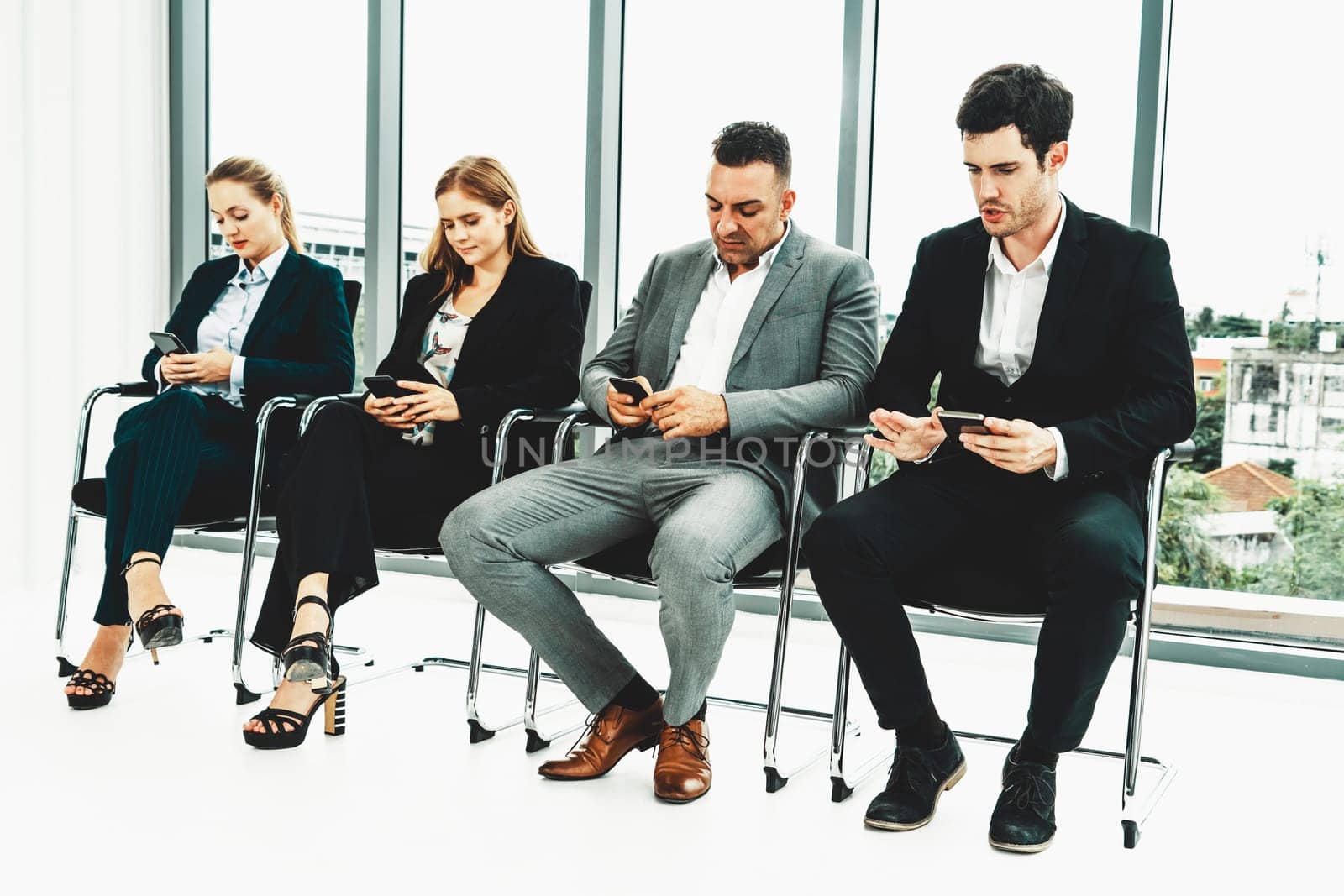 Businesswomen and businessmen using mobile phone while waiting on chairs in office for job interview. Corporate business and human resources concept. uds