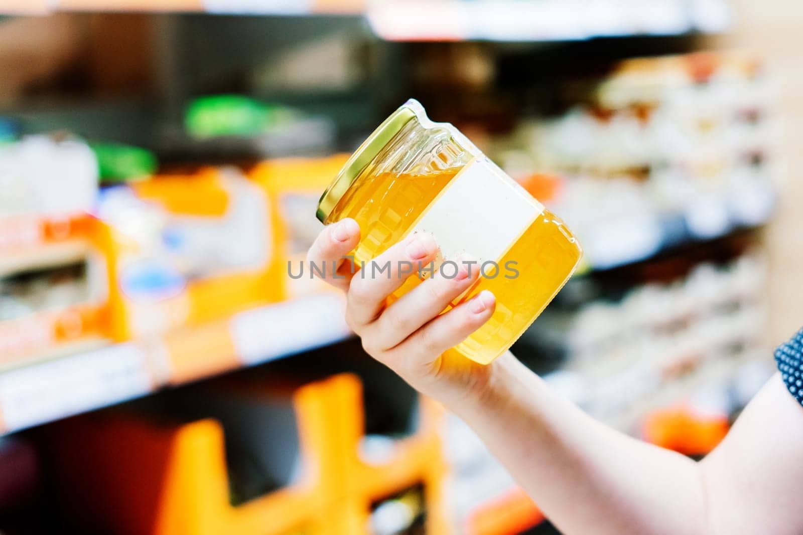 Young male hand holds honey on a blurred background, row of shelves with groceries in supermarket