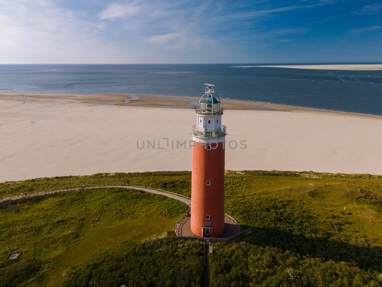 Aerial perspective of a majestic lighthouse standing tall on a sandy Texel beach, casting its guiding light over the vast expanse of the coastline.