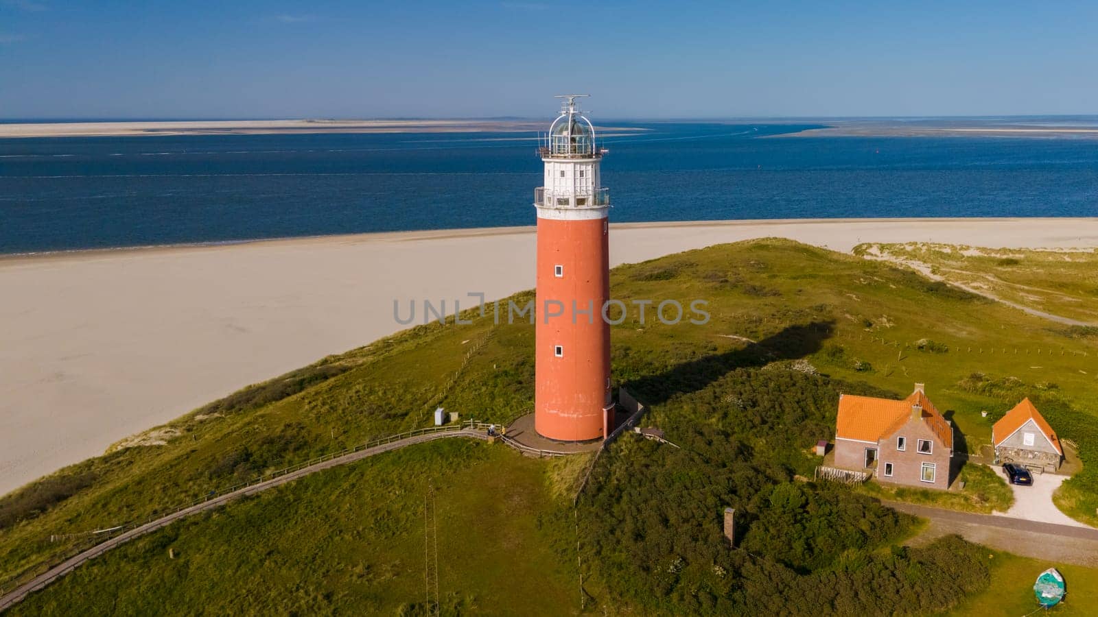 A breathtaking aerial view of a towering lighthouse standing tall on the sandy shores of Texel, Netherlands, guiding ships safely to land.