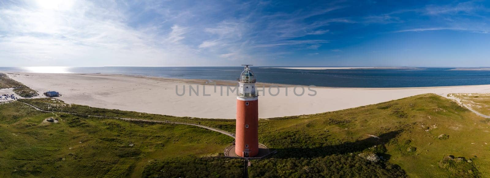 A birds eye view of a tall lighthouse with a beacon shining brightly on a sandy beach, overlooking the vast ocean on the island of Texel, Netherlands.