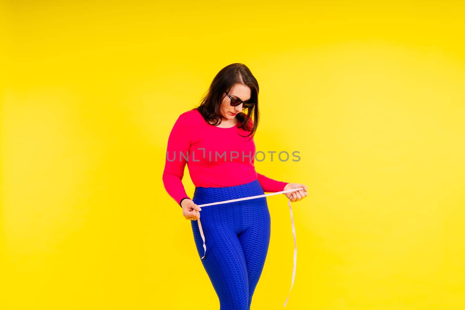 Overweight woman measuring waist before weight loss in a studio shot on yellow background