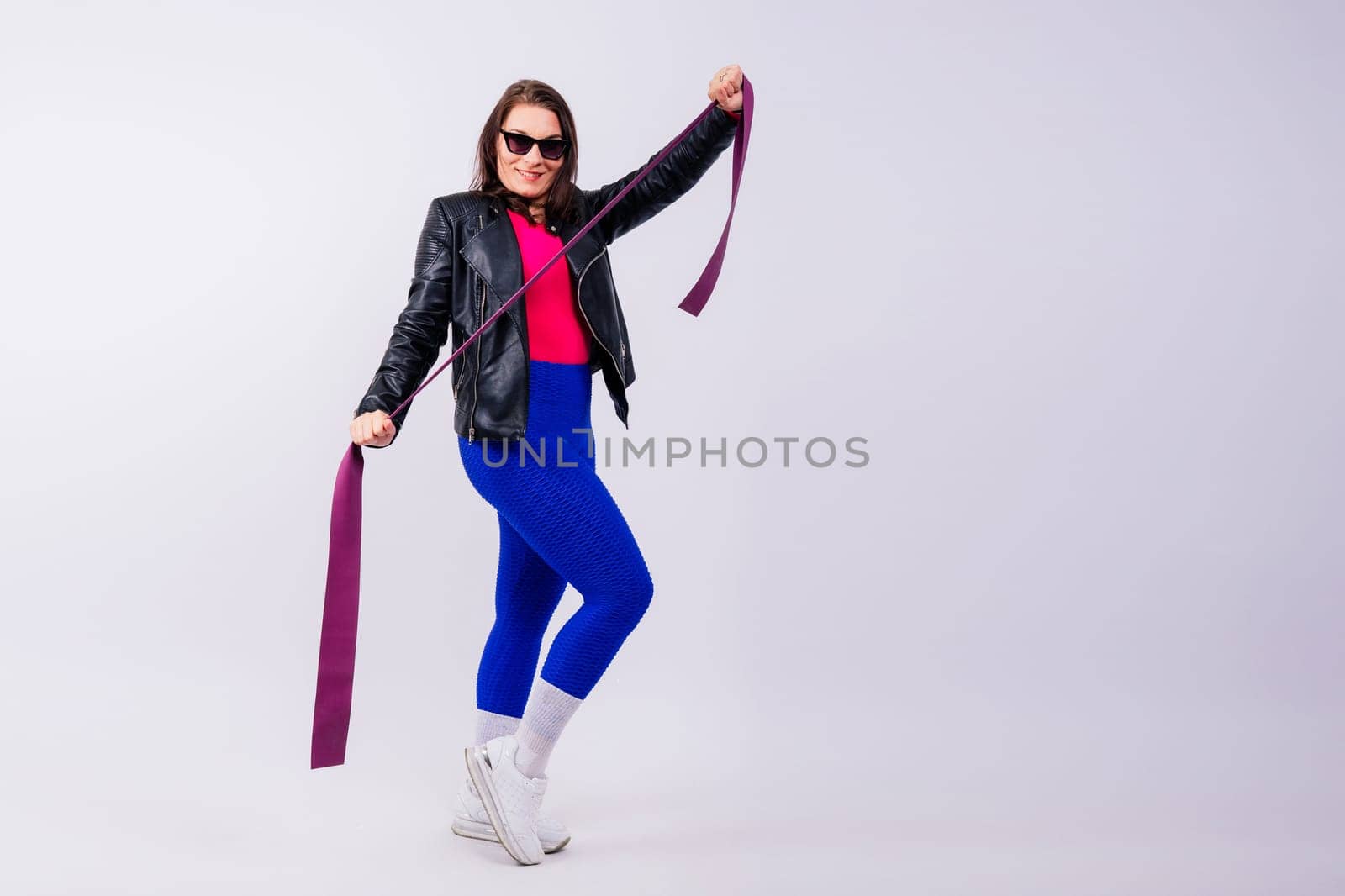 Strong female working with resistance band. Model in fashionable sportswear, grey background. by Zelenin