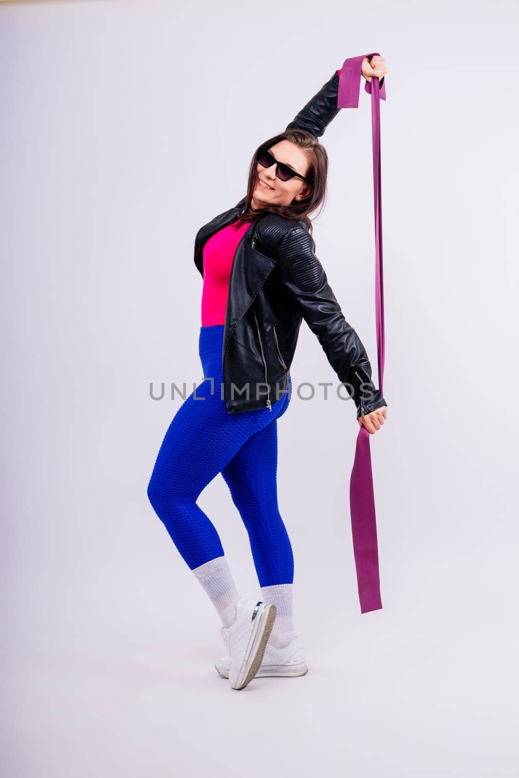 Strong female working with resistance band. Photo of model in fashionable sportswear on grey background.