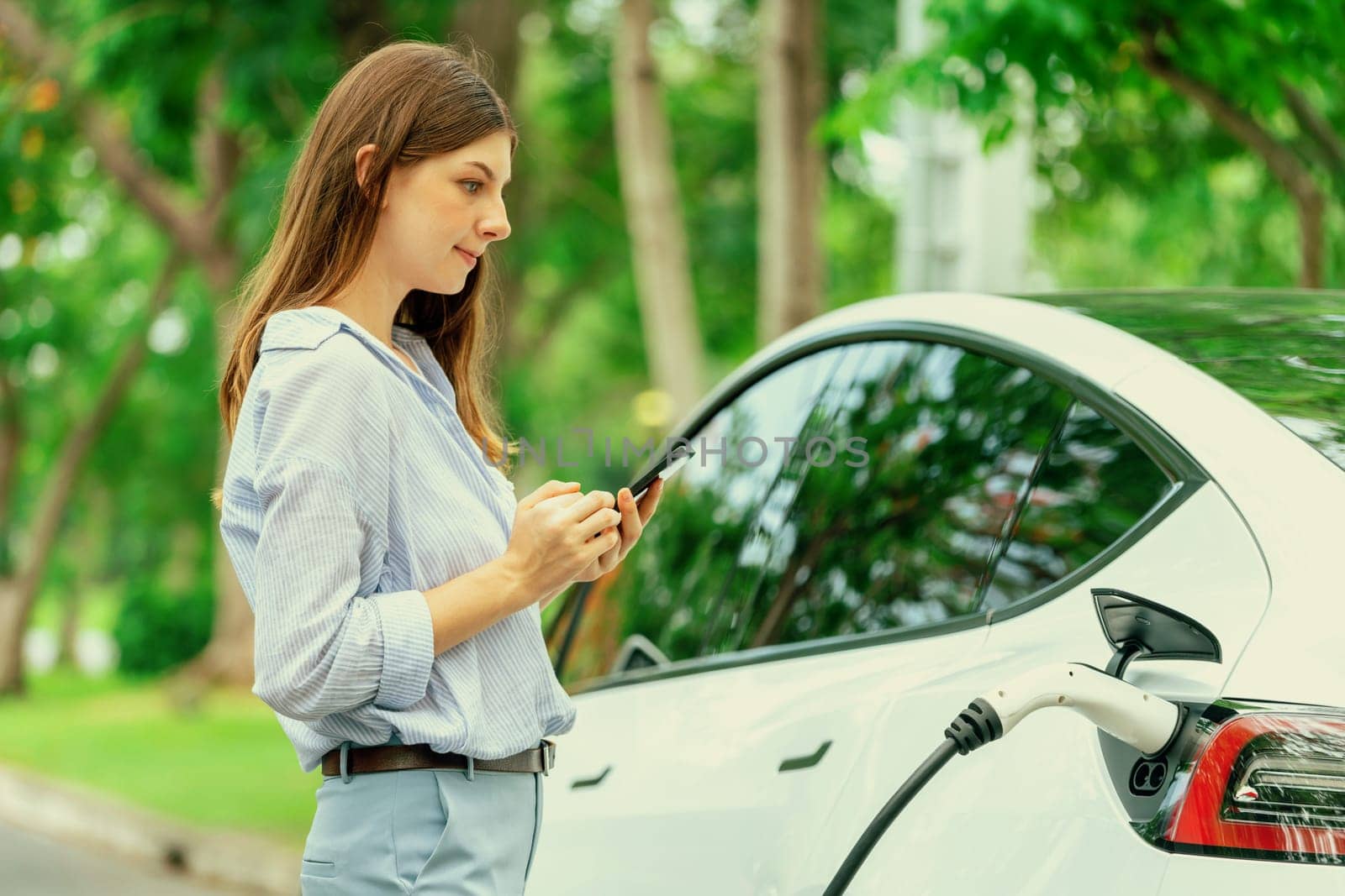 Young woman recharge EV electric vehicle battery from EV charging station. Exalt by biancoblue