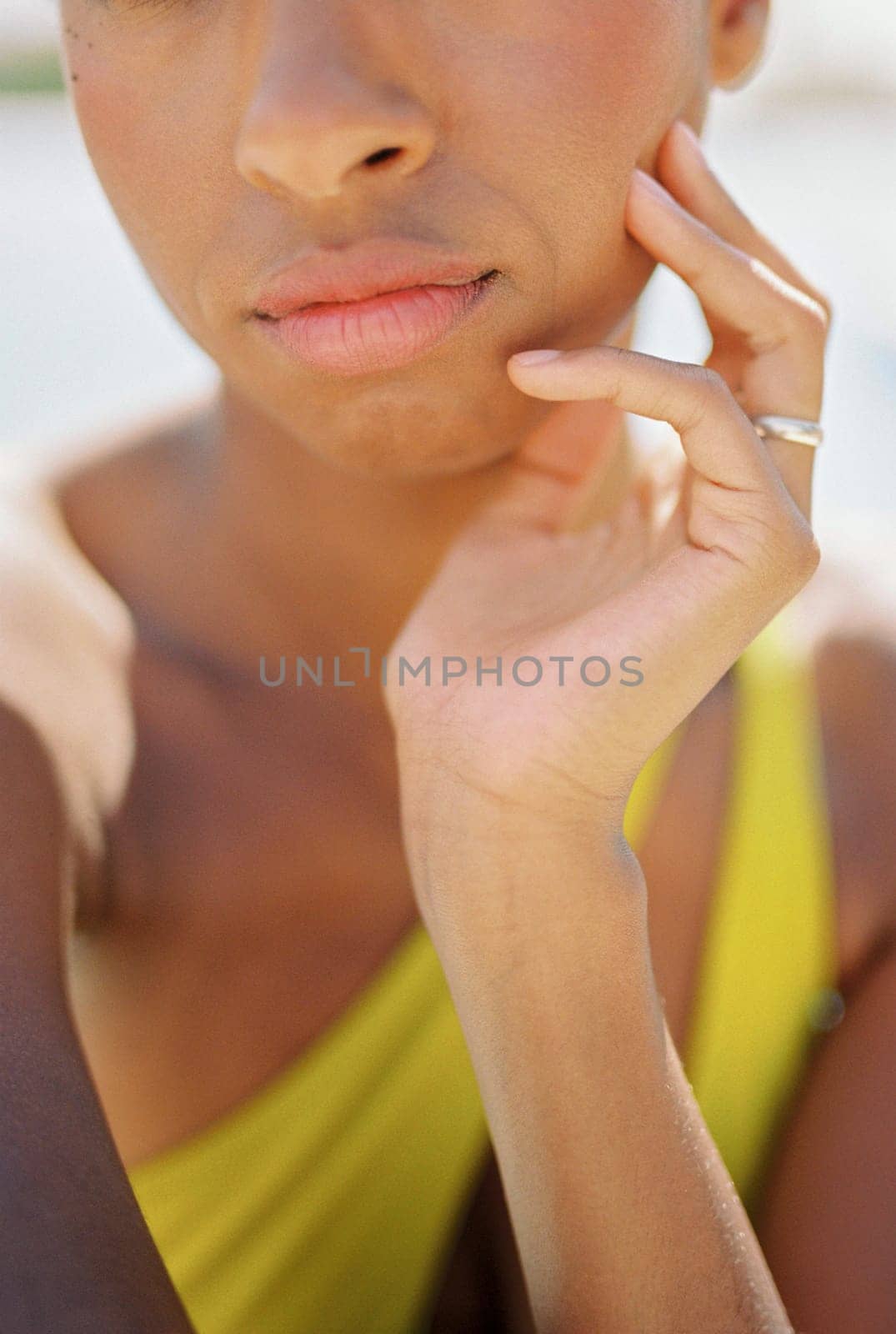 Woman in a swimsuit sits in the sun resting her chin on her hand. Cropped. High quality photo
