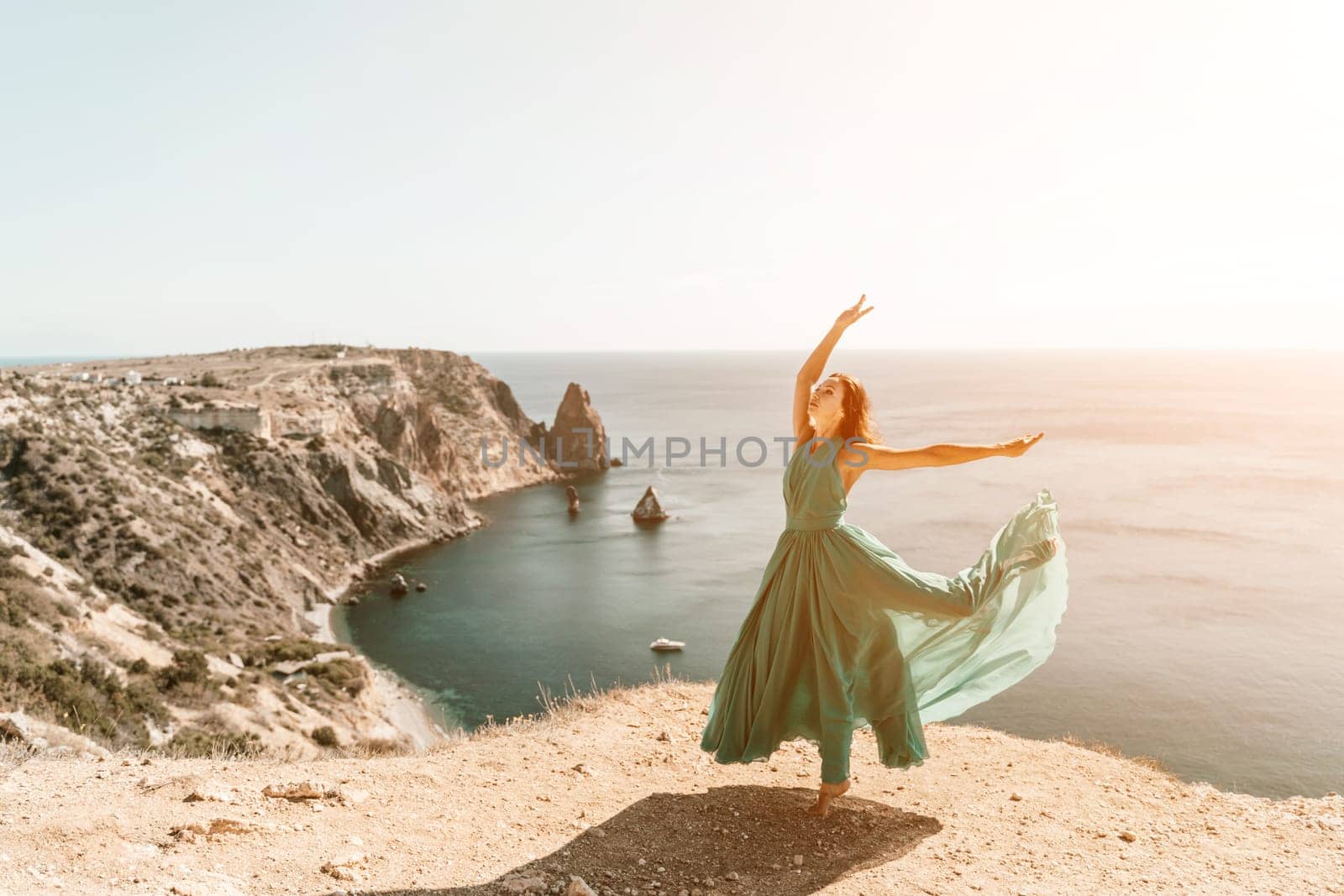 Woman green dress sea. Female dancer posing on a rocky outcrop high above the sea. Girl on the nature on blue sky background. Fashion photo