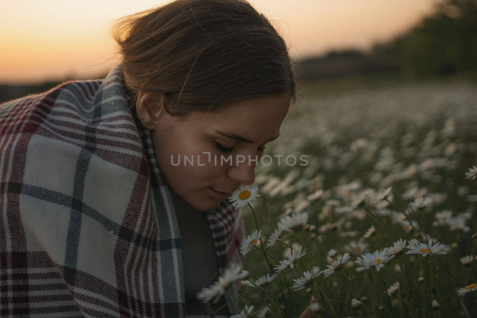 A woman is sniffing a flower in a field. The scene is peaceful and serene, with the woman enjoying the beauty of nature