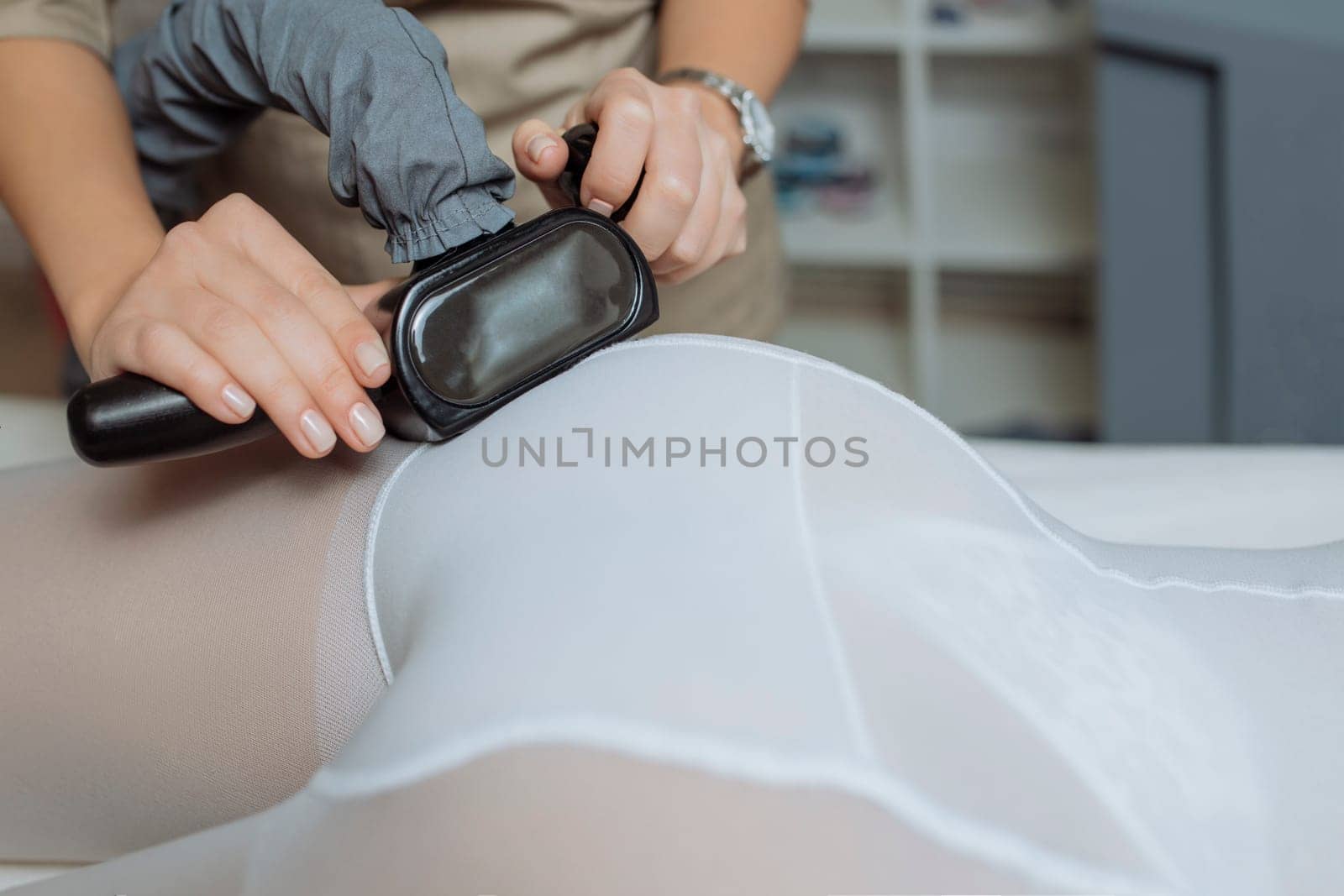 Close up shot of therapist beautician makes LPG massage treatment to young woman in white transparent suit, lying at beauty SPA clinic. Focus on hands holding medical unit by malyshph