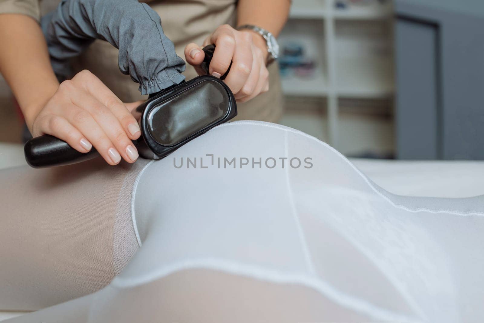 Close up shot of therapist beautician makes LPG massage treatment to young woman in white transparent suit, lying at beauty SPA clinic. Focus on hands holding medical unit.