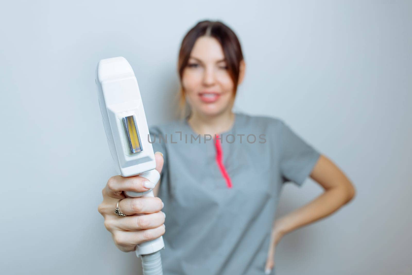 Female cosmetologist in a medical coat holds a working part of the modern laser epilator in her hands and poses for a photo. Laser epilation treatment in cosmetic beauty clinic. by malyshph