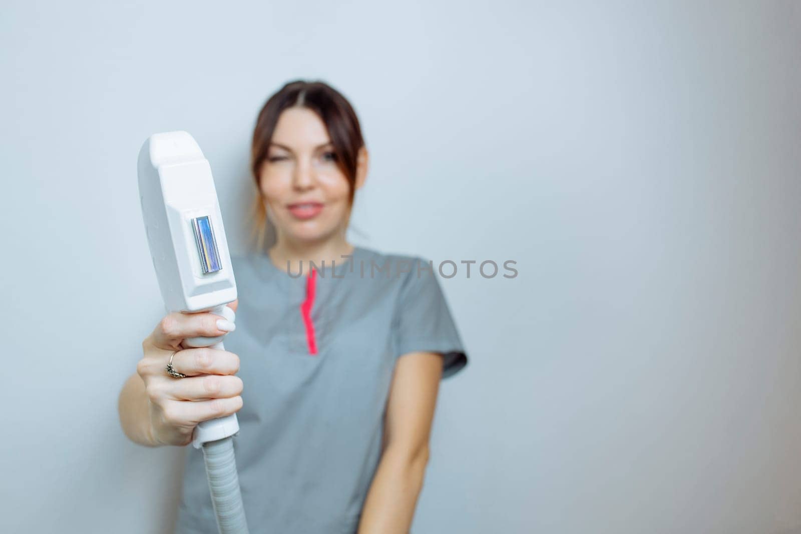 Female cosmetologist in a medical coat holds a working part of the modern laser epilator in her hands and poses for a photo. Laser epilation treatment in cosmetic beauty clinic