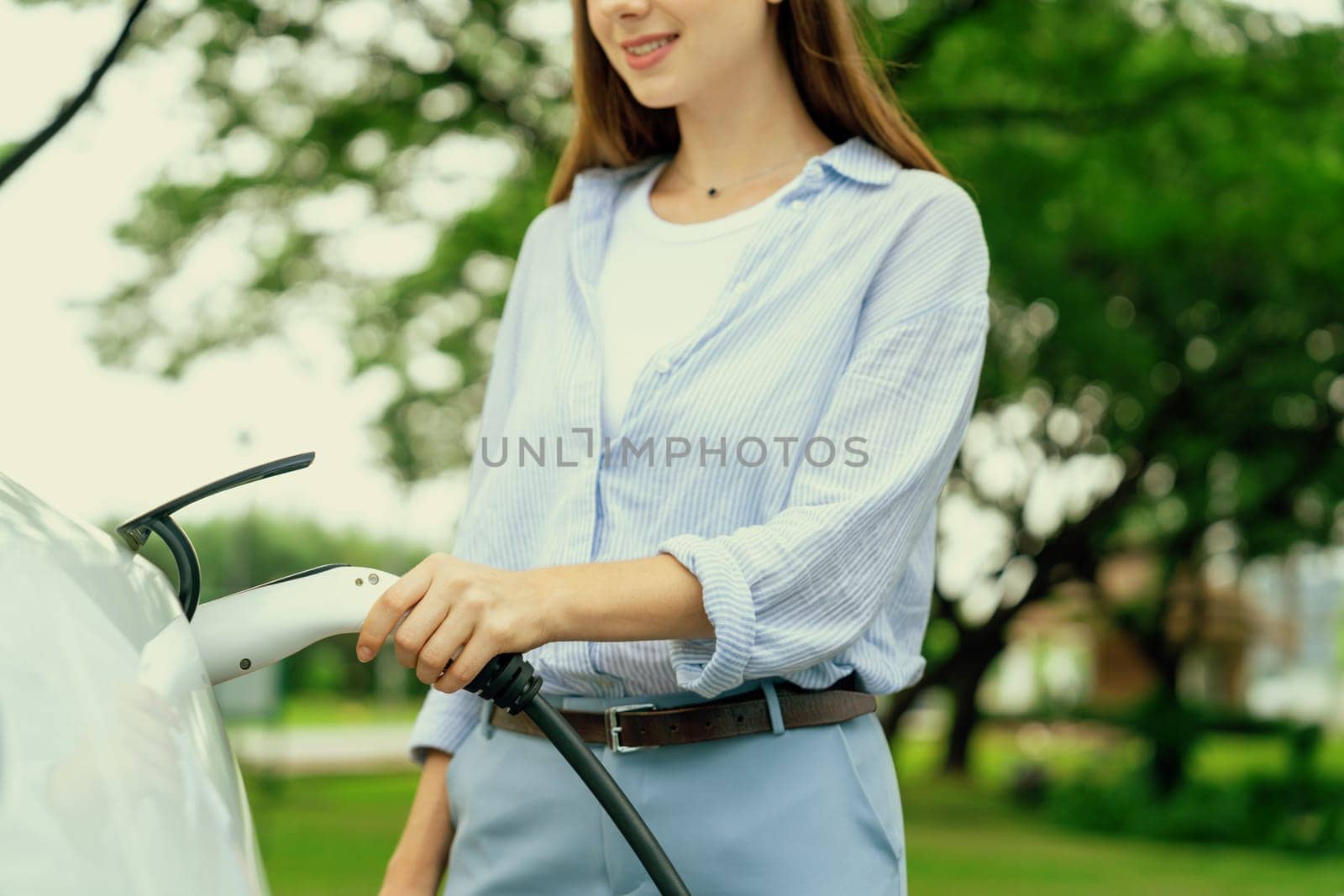 Young woman recharge EV electric vehicle battery from EV charging station. Exalt by biancoblue