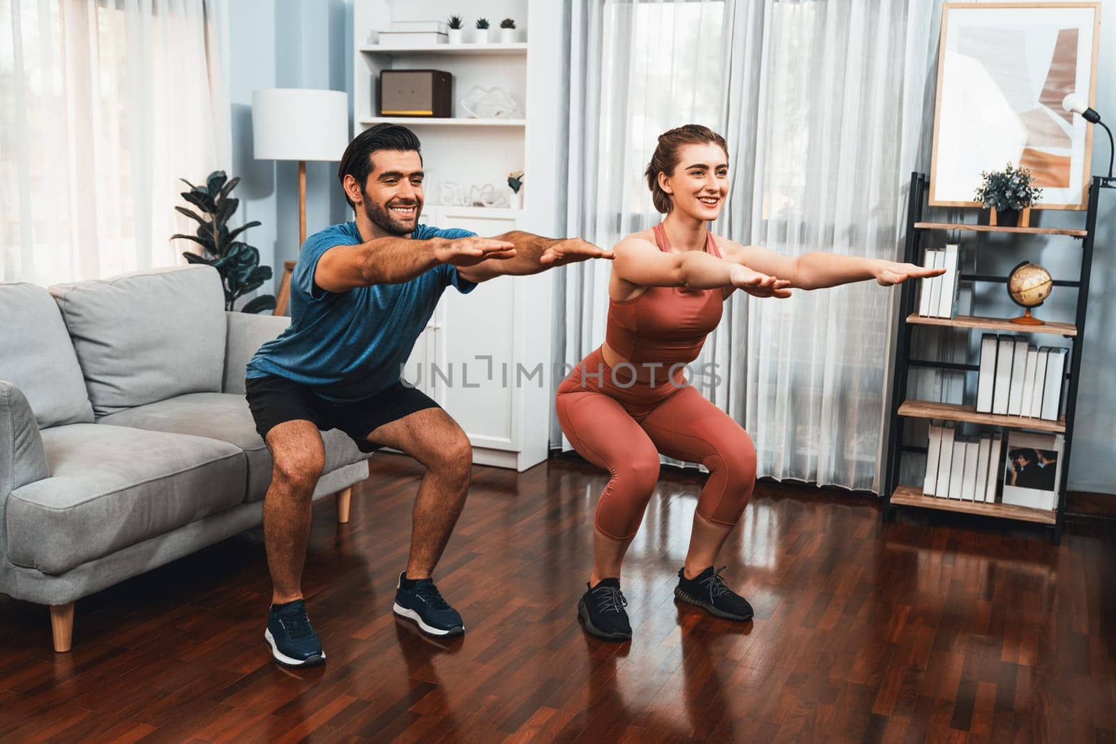 Athletic and sporty couple doing squat together during home body workout exercise session for fit physique and healthy sport lifestyle at home. Gaiety home exercise workout training concept.