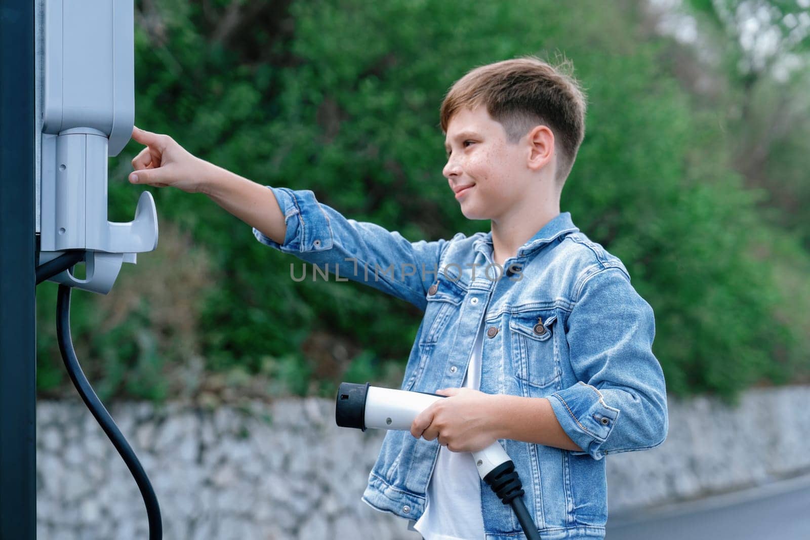 Little boy recharging eco-friendly electric car from EV charging station. EV car road trip travel concept for alternative transportation powered by clean renewable and sustainable energy. Perpetual