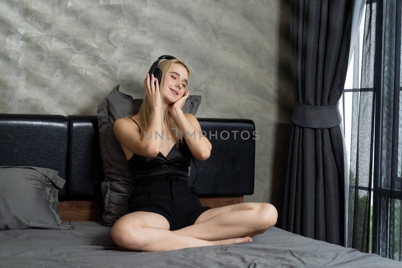 Young woman listening to music on headphone on her bed. Blithe by biancoblue