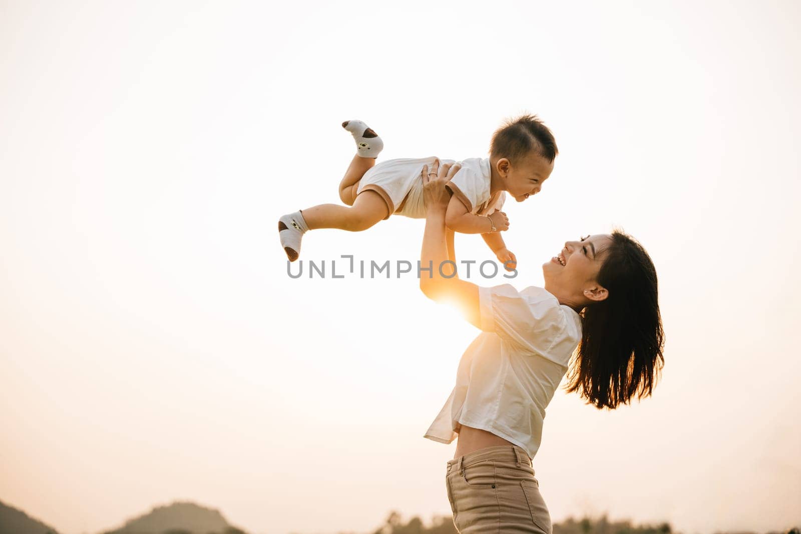 A woman holds her newborn baby up high by Sorapop