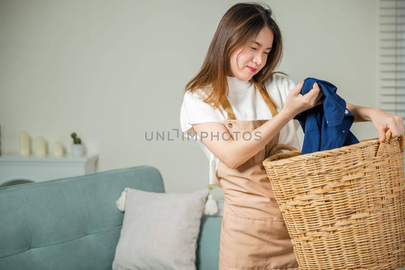 Happy housewife woman holding basket with heap of different clothes on sofa by Sorapop