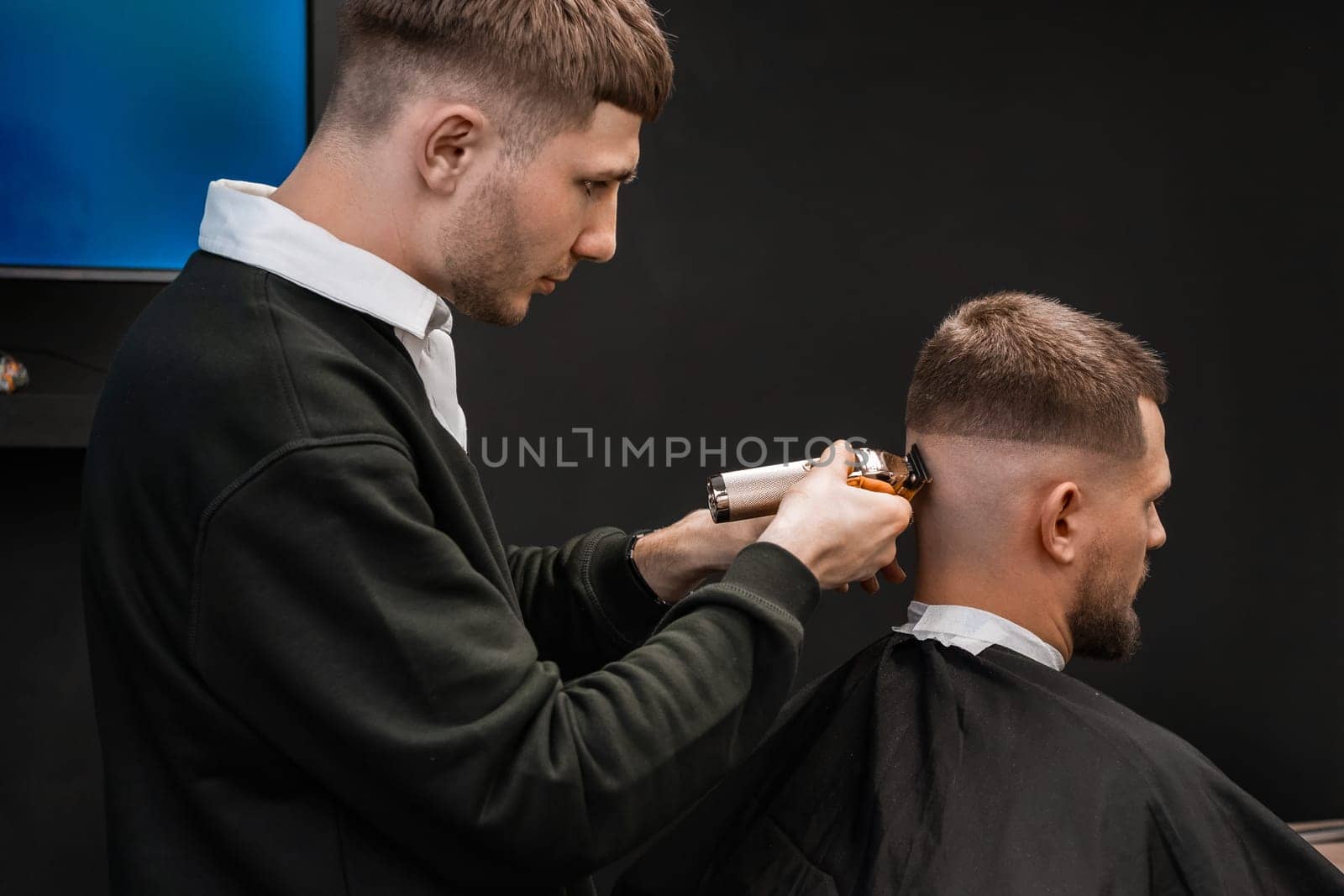 Young barber skillfully uses a trimmer to cut a mans hair