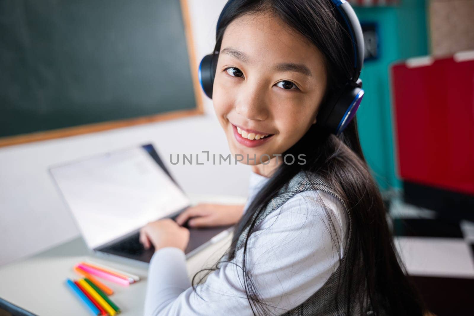 A young girl is sitting at a desk with a laptop and a book by Sorapop