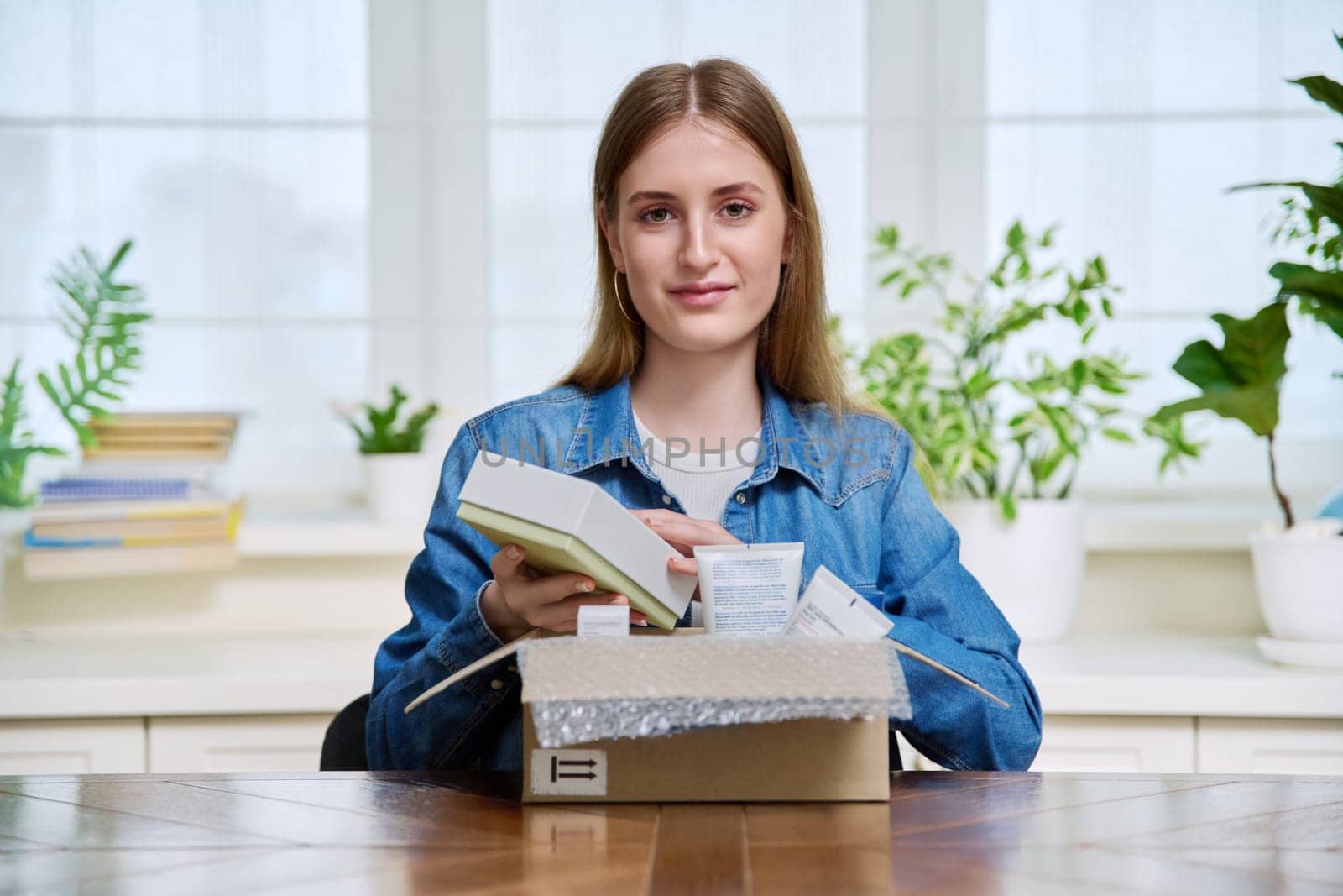 Satisfied young female customer buyer sitting at home unpacking cardboard box with online purchases. Teenage girl unpacking boxes with cosmetics care products perfumes. Delivery by mail, online store