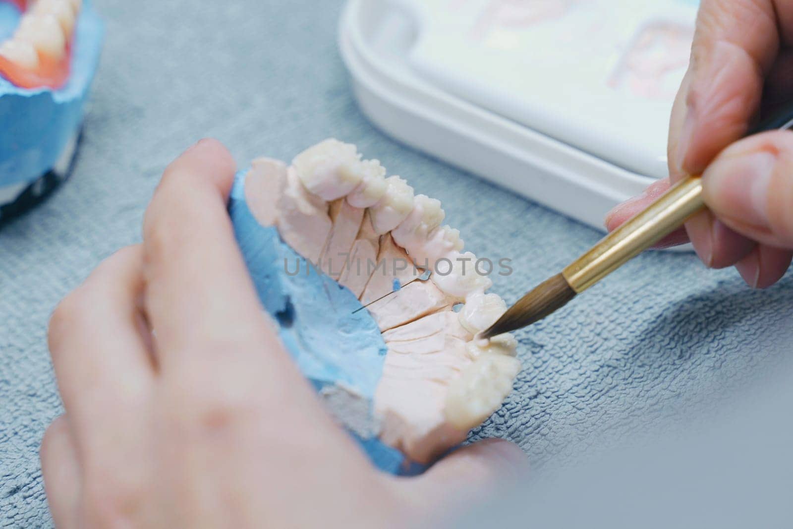 Dental technician coloring dental prosthesis with a paint brush at the laboratory, close-up view. Concept of implantats producing