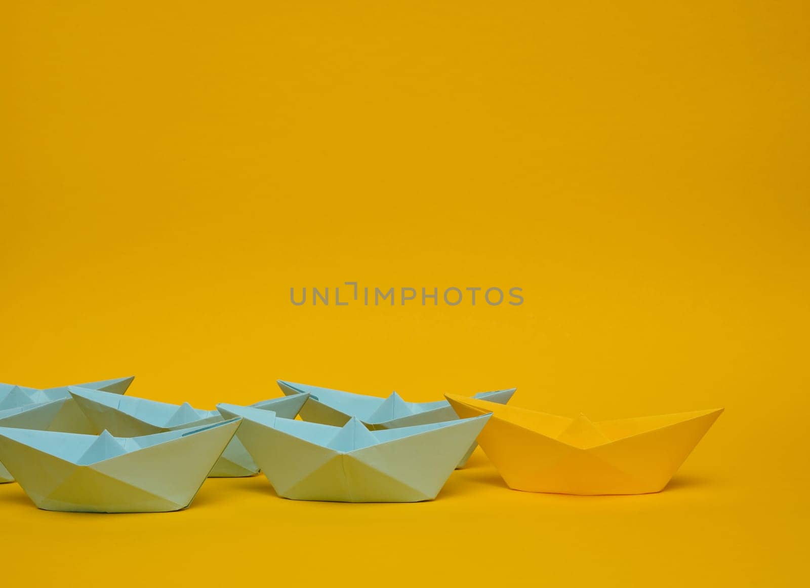 Group of blue paper boats follow yellow against a yellow background. Strong leader concept, mass manipulation. Starting a business with a well-coordinated team, start-up