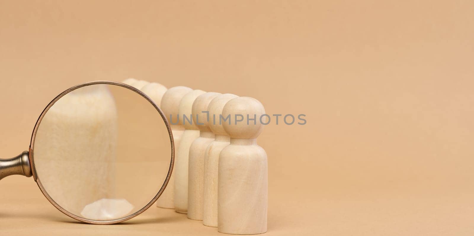 Wooden figures of men stand on a beige background and a wooden magnifying glass. Recruitment concept, search for talented and capable employees, career growth