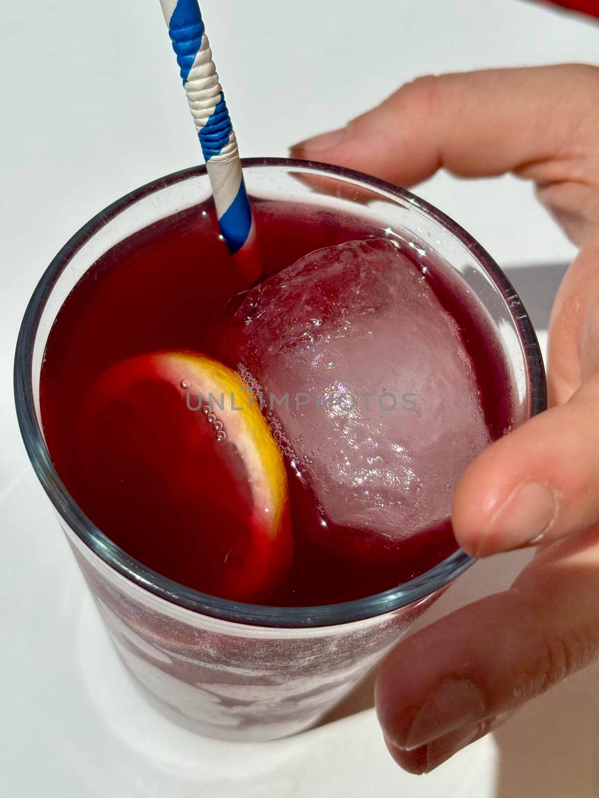 Holding glass of red sangria, Tinto de Verano, top view on white table. High quality photo