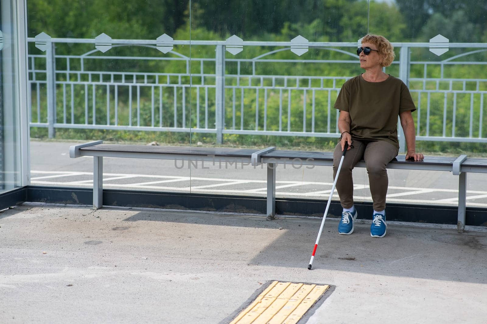 An elderly blind woman is waiting for transport at a bus stop