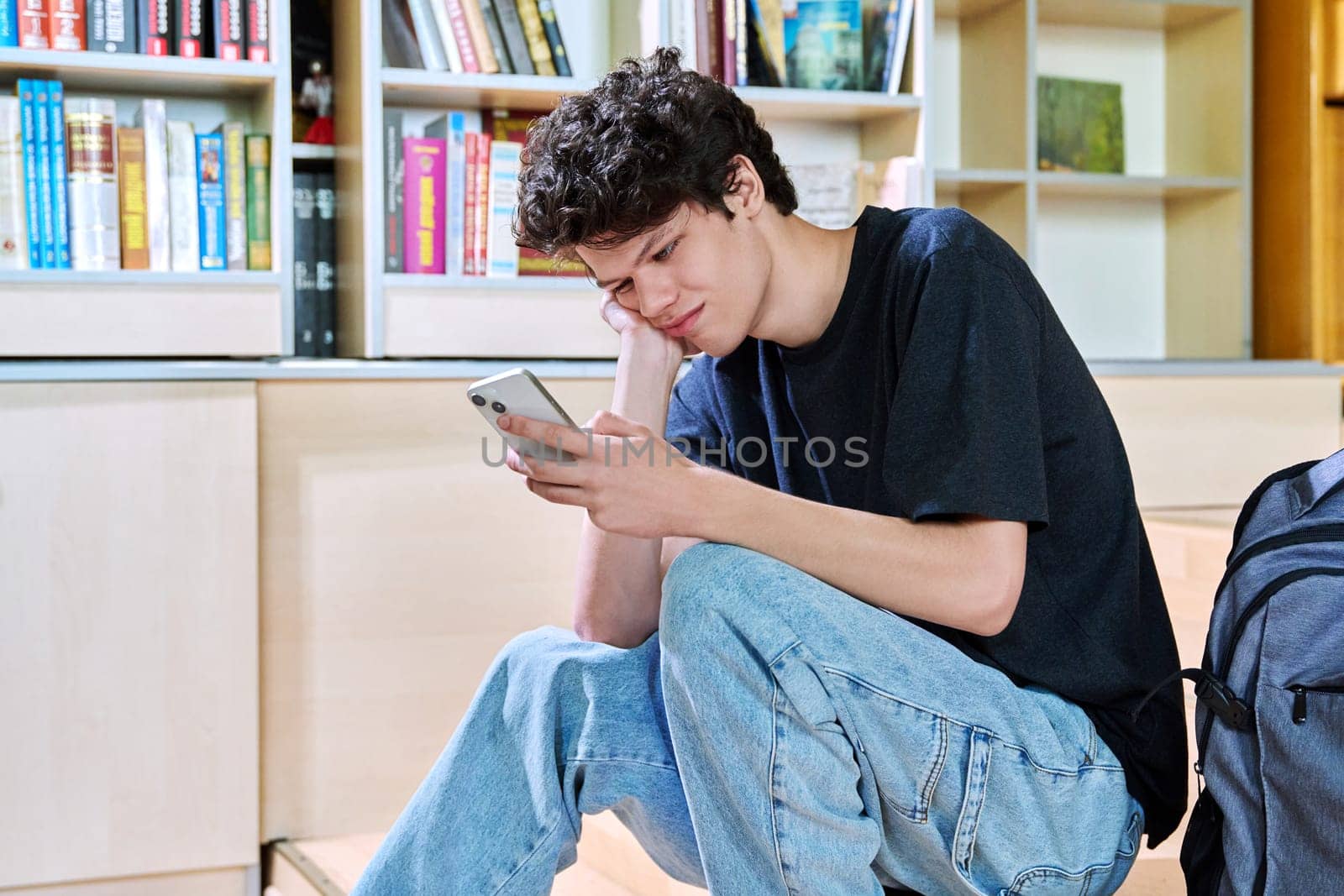 Sad upset young male college student looking at smartphone while sitting in classroom. Negative emotions, difficulties, troubles, youth concept